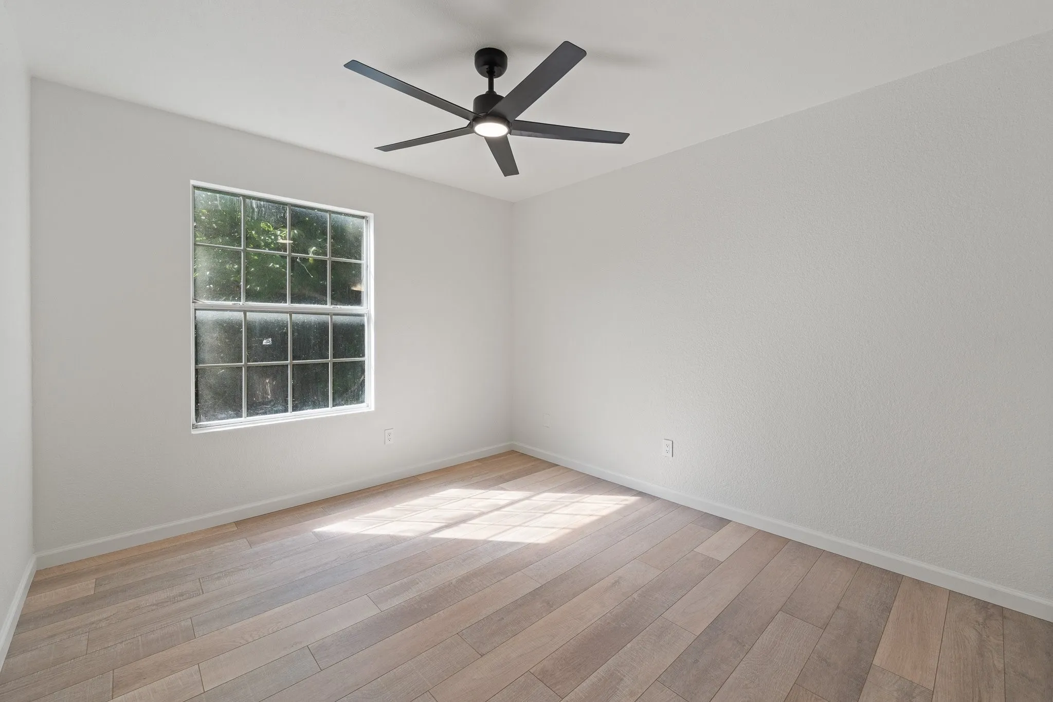Room featuring light wood-finish flooring, white walls, and a multi-pane window