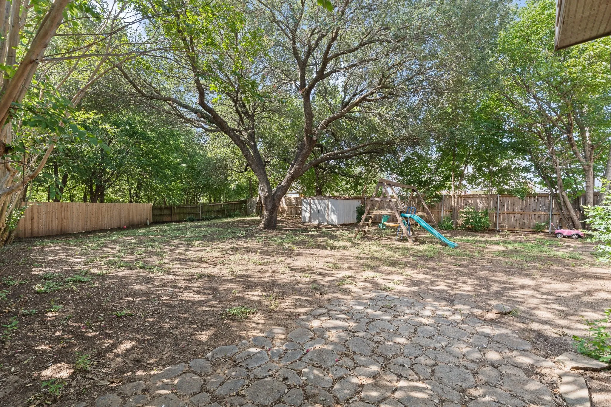 Expansive backyard featuring mature trees, a privacy fence, and a stone patio