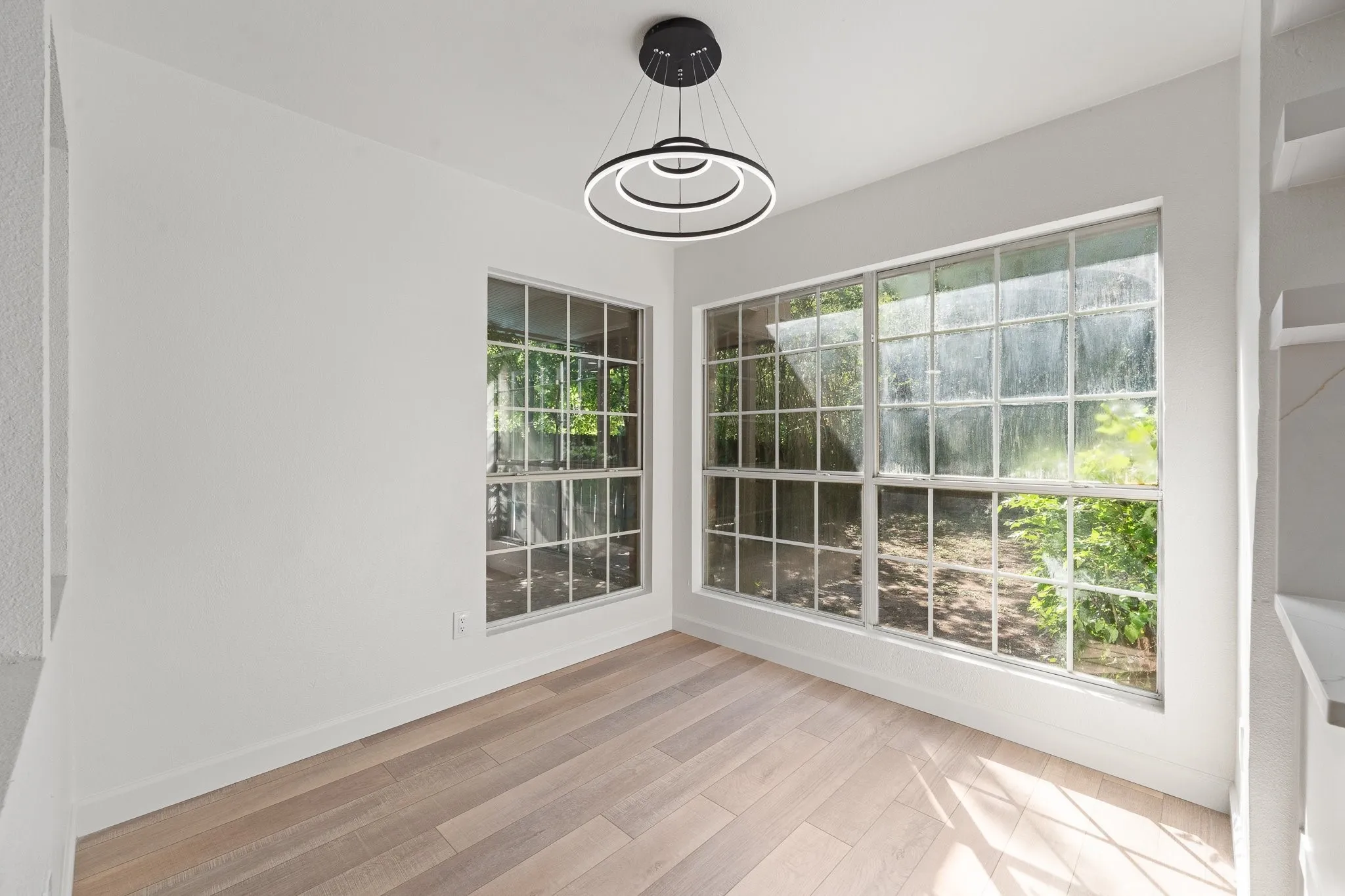 Spacious room featuring light wood-finish flooring, white baseboards, and a modern circular chandelier