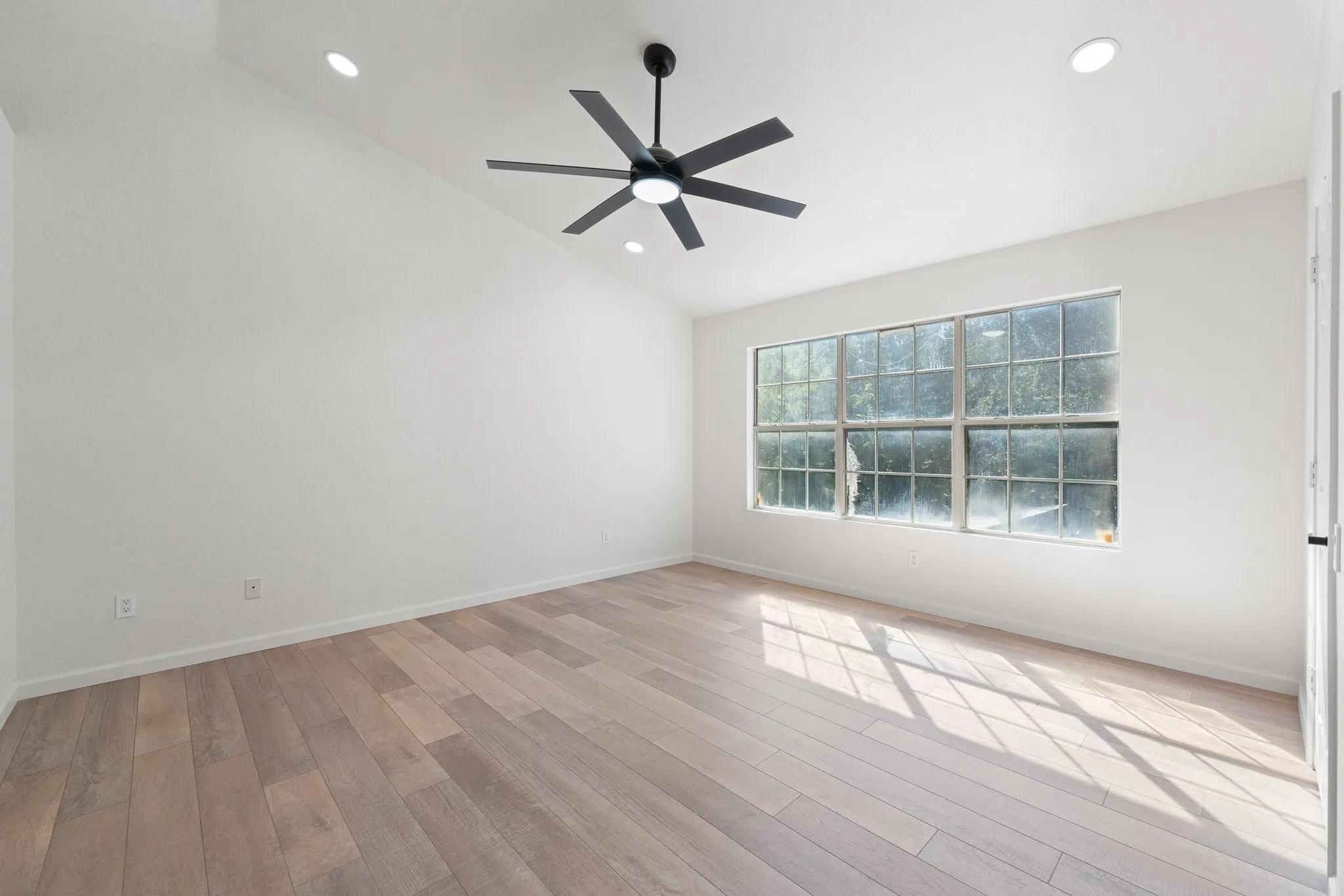 Bright interior space featuring a large window with multiple panes, wood-finish flooring, a modern ceiling fan, recessed lighting, and a vaulted ceiling