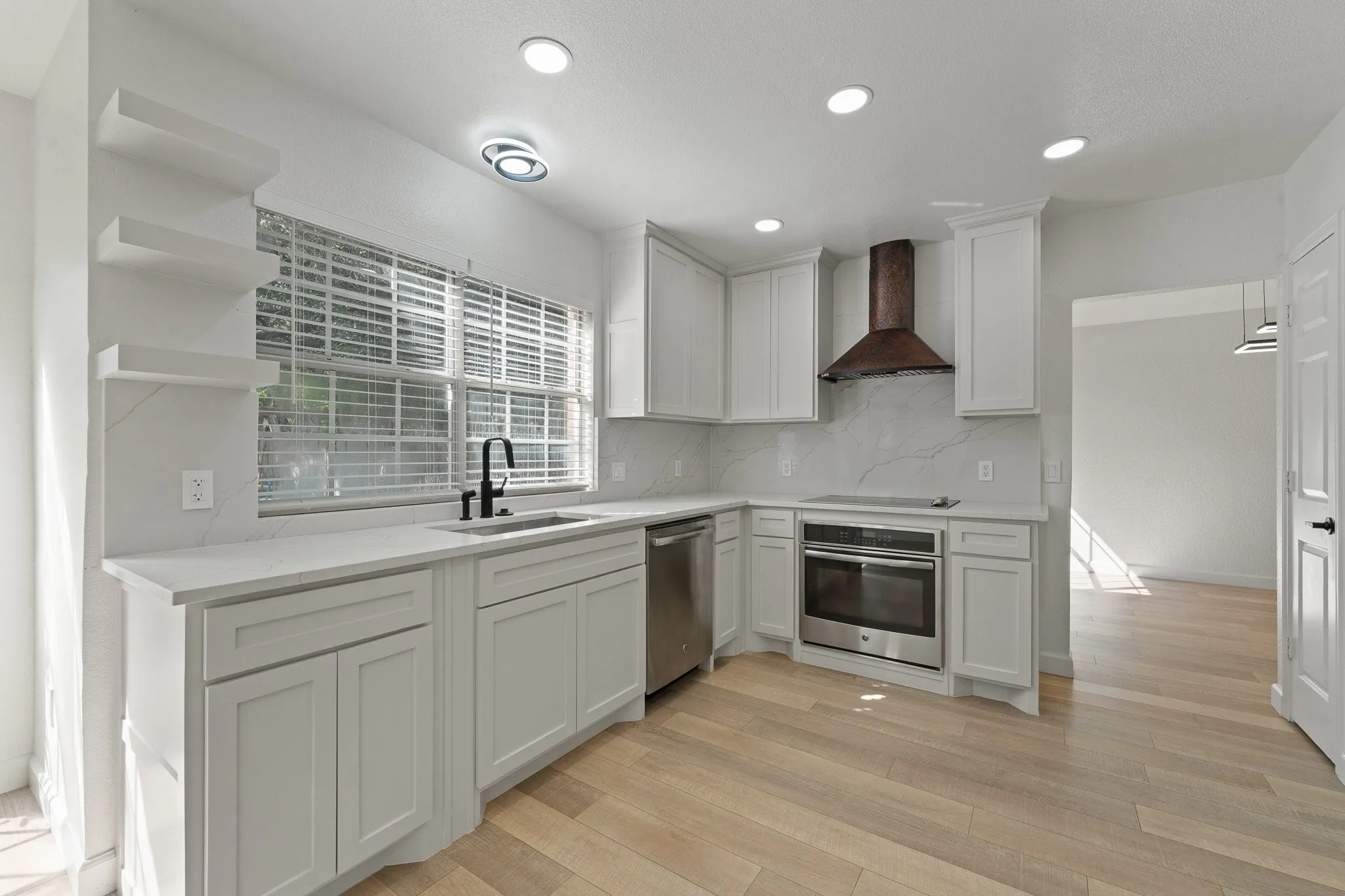 Modern kitchen featuring white shaker cabinetry, light wood-finish flooring, a stainless steel oven, and a contemporary range hood