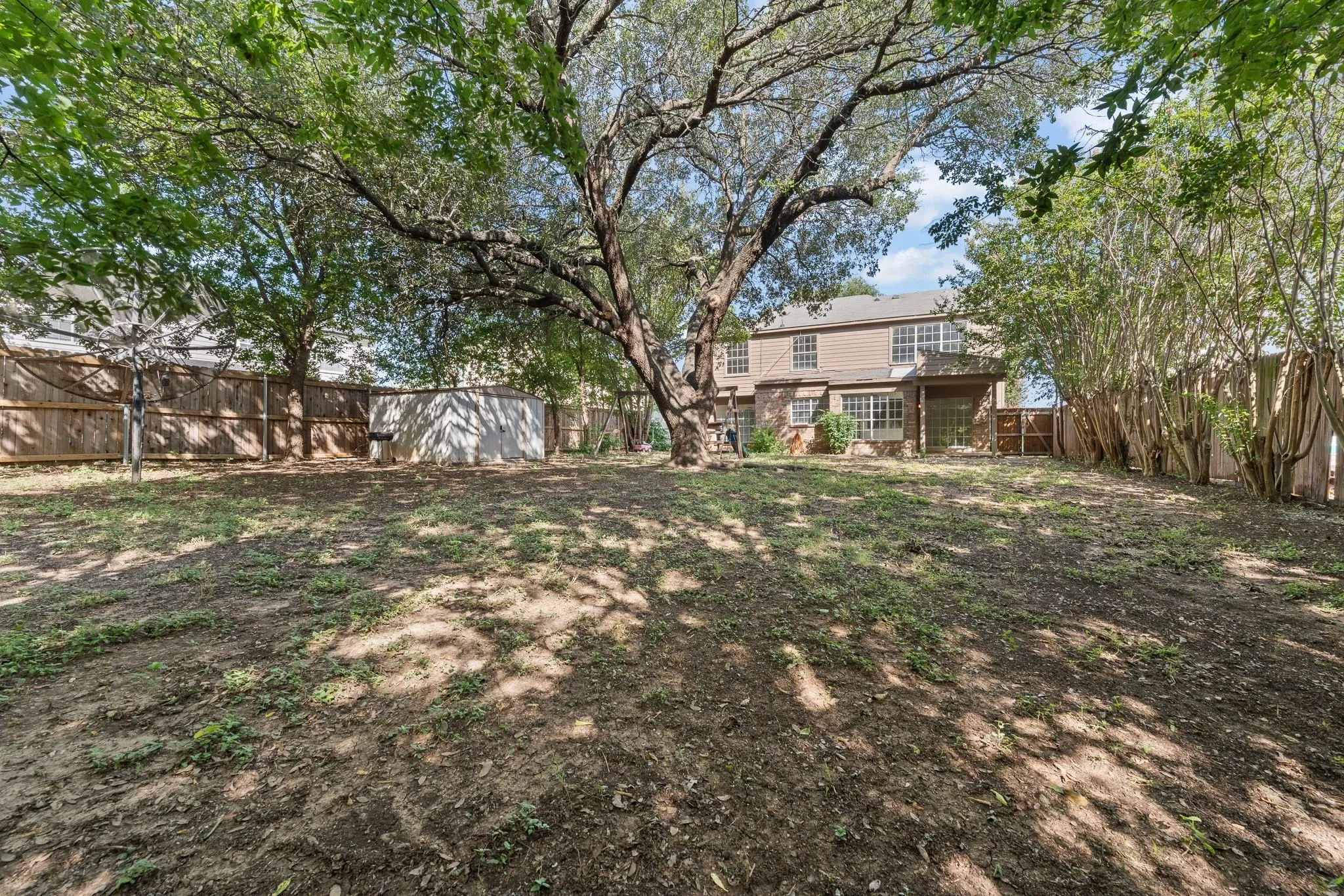 Expansive rear yard featuring a mature shade tree, a wood privacy fence, and a two-story residence with a covered patio