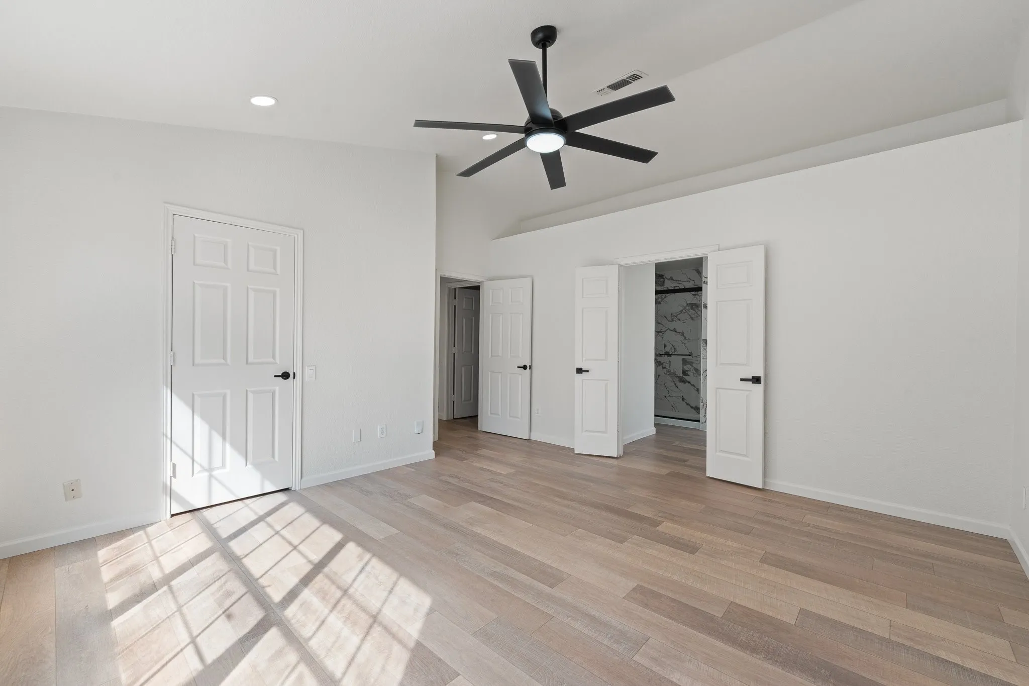 Spacious room featuring wood-finish flooring, vaulted ceilings, and a contemporary black ceiling fan with integrated lighting