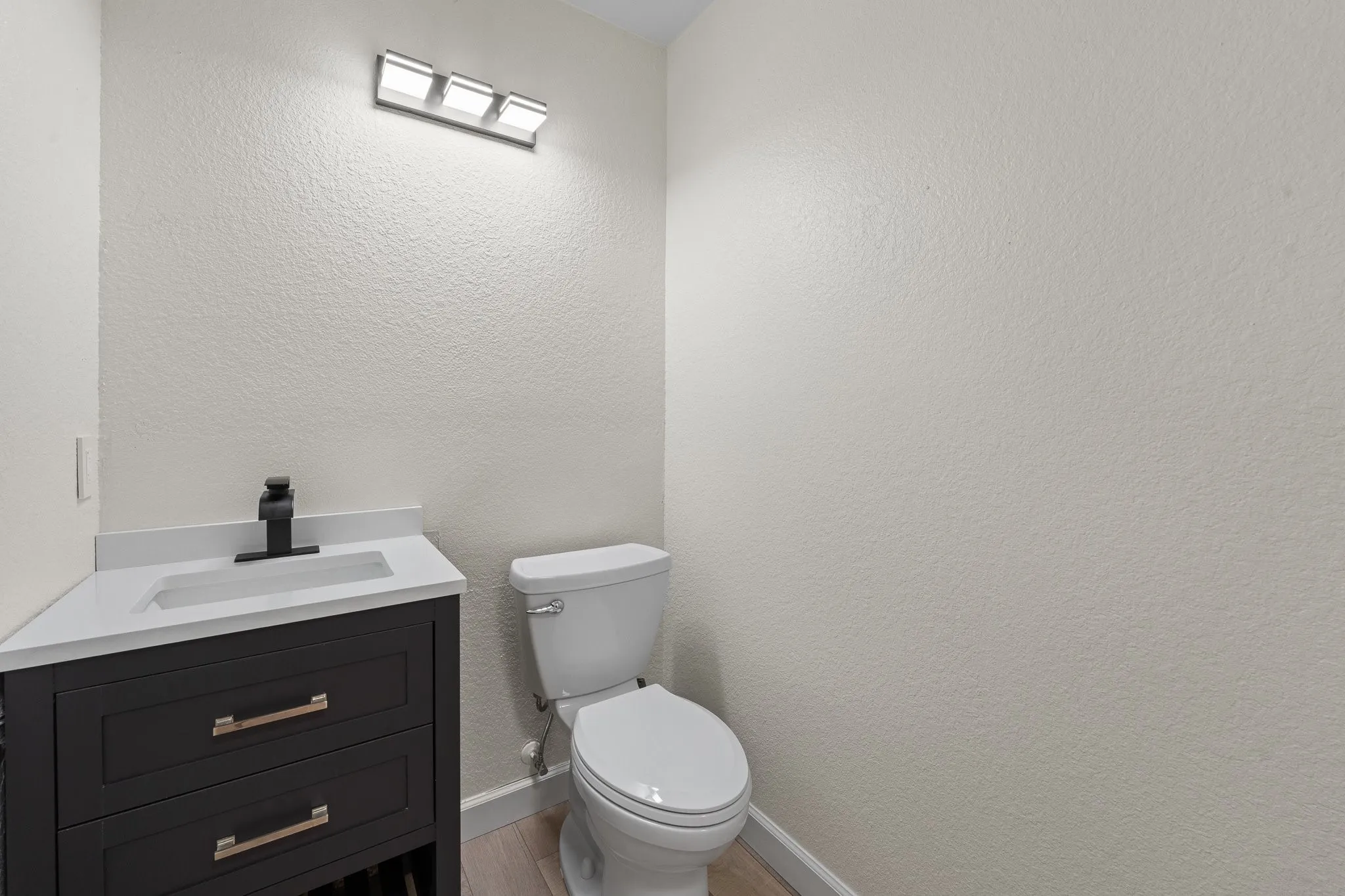Modern vanity with a white countertop and integrated sink, matte black faucet, and rectangular sconce lighting fixture