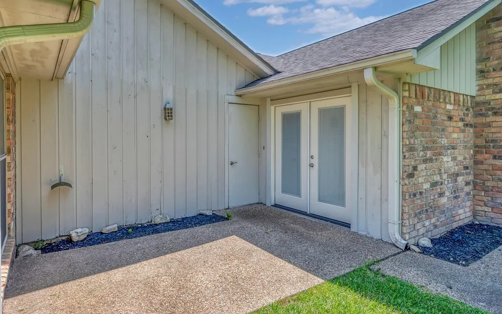 Exterior featuring board and batten siding, brick accents, and a dual pane glass door entry