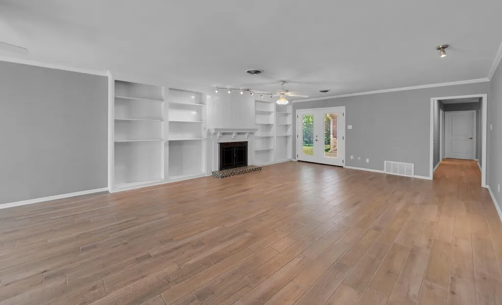 Spacious living area featuring wood-finish flooring, built-in shelving, a central fireplace with decorative mantel, and French doors