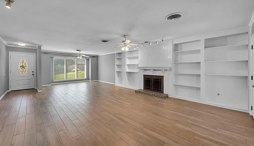 Spacious room featuring wood-finish flooring, a decorative front entry door with an oval glass insert, and a fireplace with a decorative tile hearth