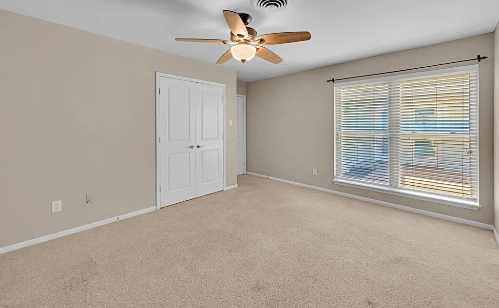 Carpeted room featuring neutral wall tones, a ceiling fan with integrated lighting, a double window with blinds, and white bi-fold closet doors