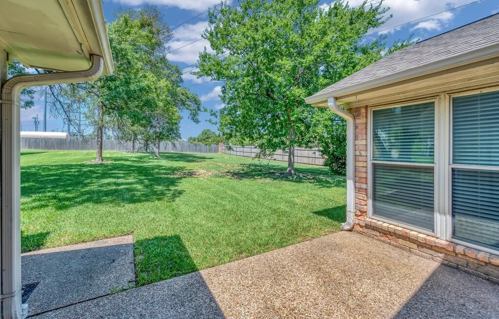 Expansive grassy backyard featuring mature trees, a wood privacy fence, and a concrete patio