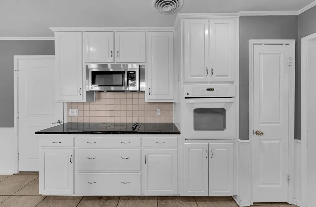 Kitchen featuring white cabinetry with brushed nickel hardware, a built-in stainless steel microwave, black cooktop, and a matching built-in white oven