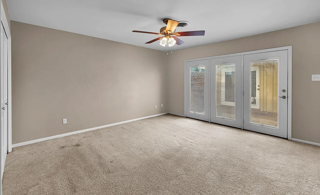 Carpeted room featuring a ceiling fan with integrated lighting, a door with white trim, and a three-panel glass-paned exterior door