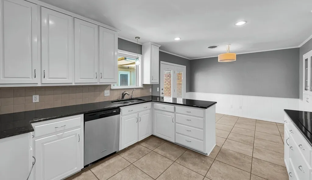 Spacious kitchen featuring extensive white cabinetry, dark countertops, a built-in stainless steel dishwasher, and a tile backsplash