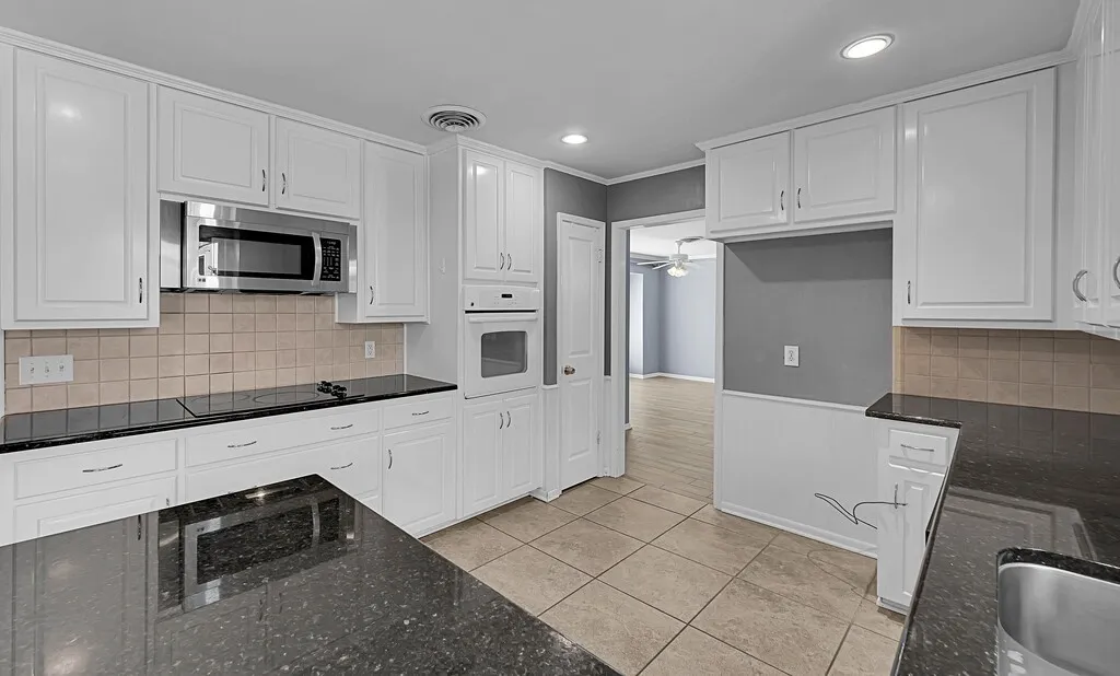 Kitchen featuring white cabinetry, dark speckled countertops, and a tiled backsplash