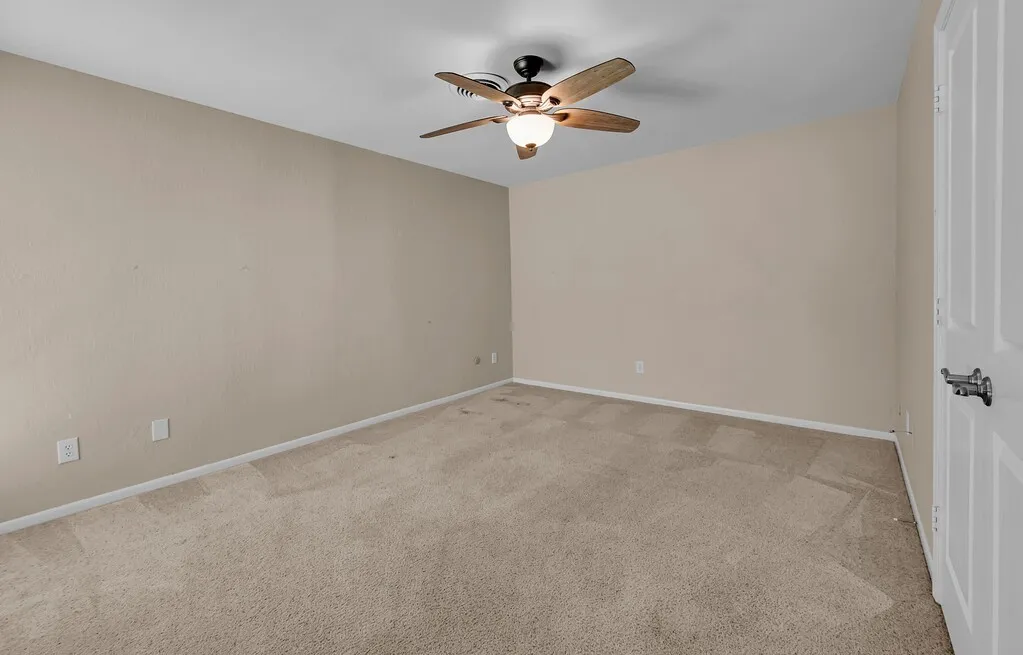 Spacious room featuring neutral carpeting, light beige wall paint, white trim, and a ceiling fan with integrated lighting