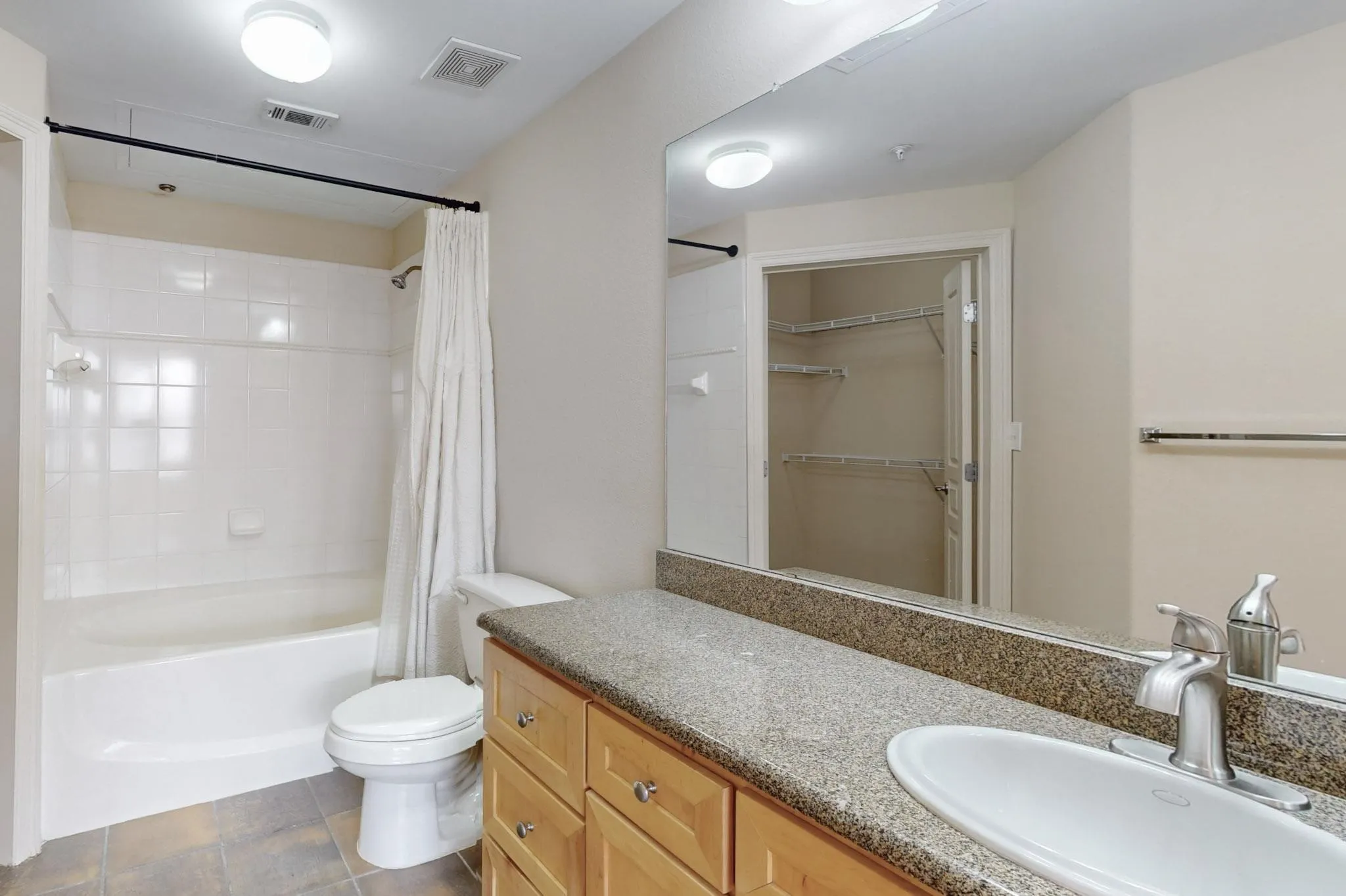 Bathroom with shower / bathtub combination with curtain, vanity, a walk in closet, and dark tile patterned floors
