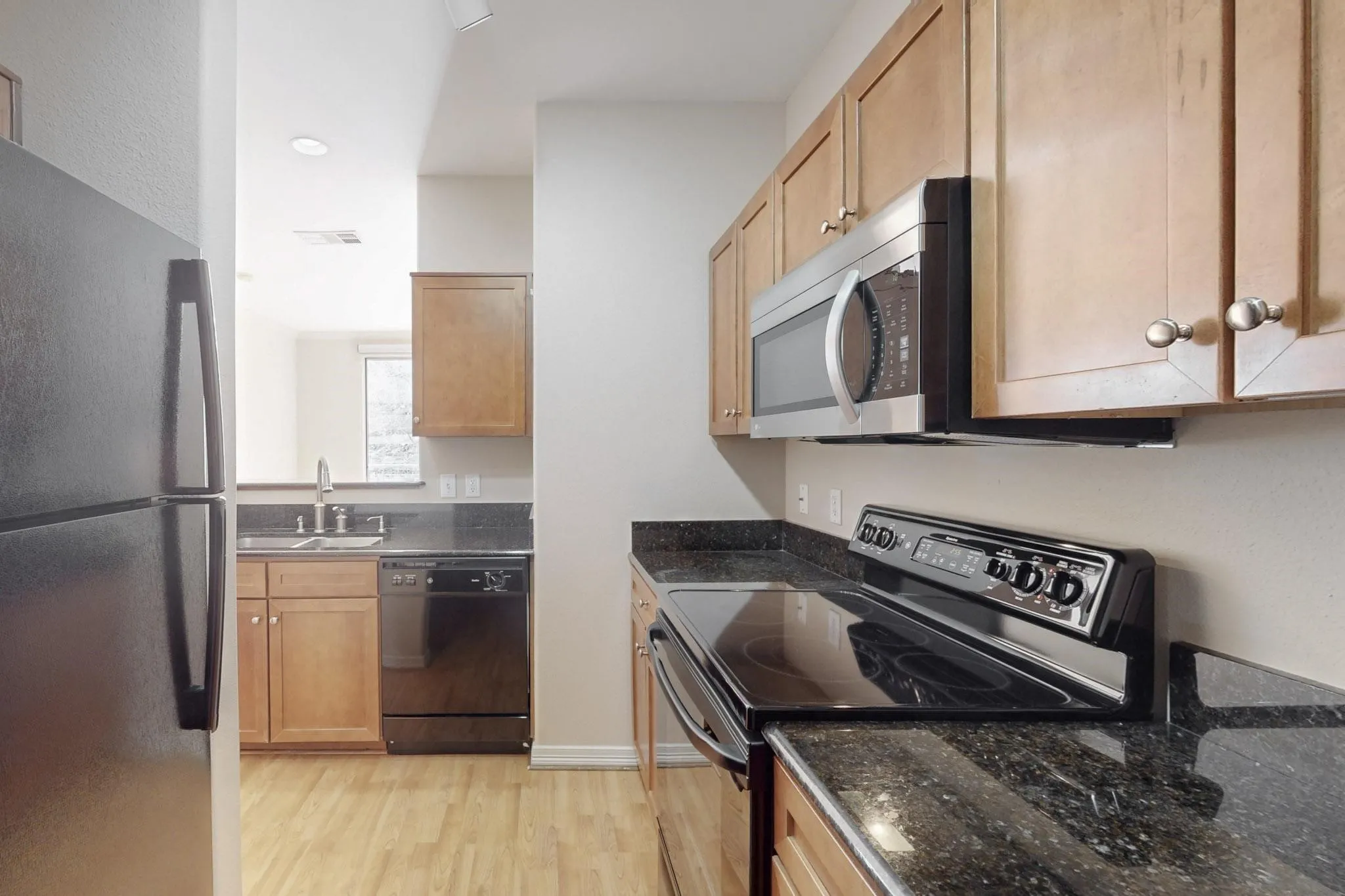 Kitchen featuring black appliances, light wood finished floors, and dark stone counters