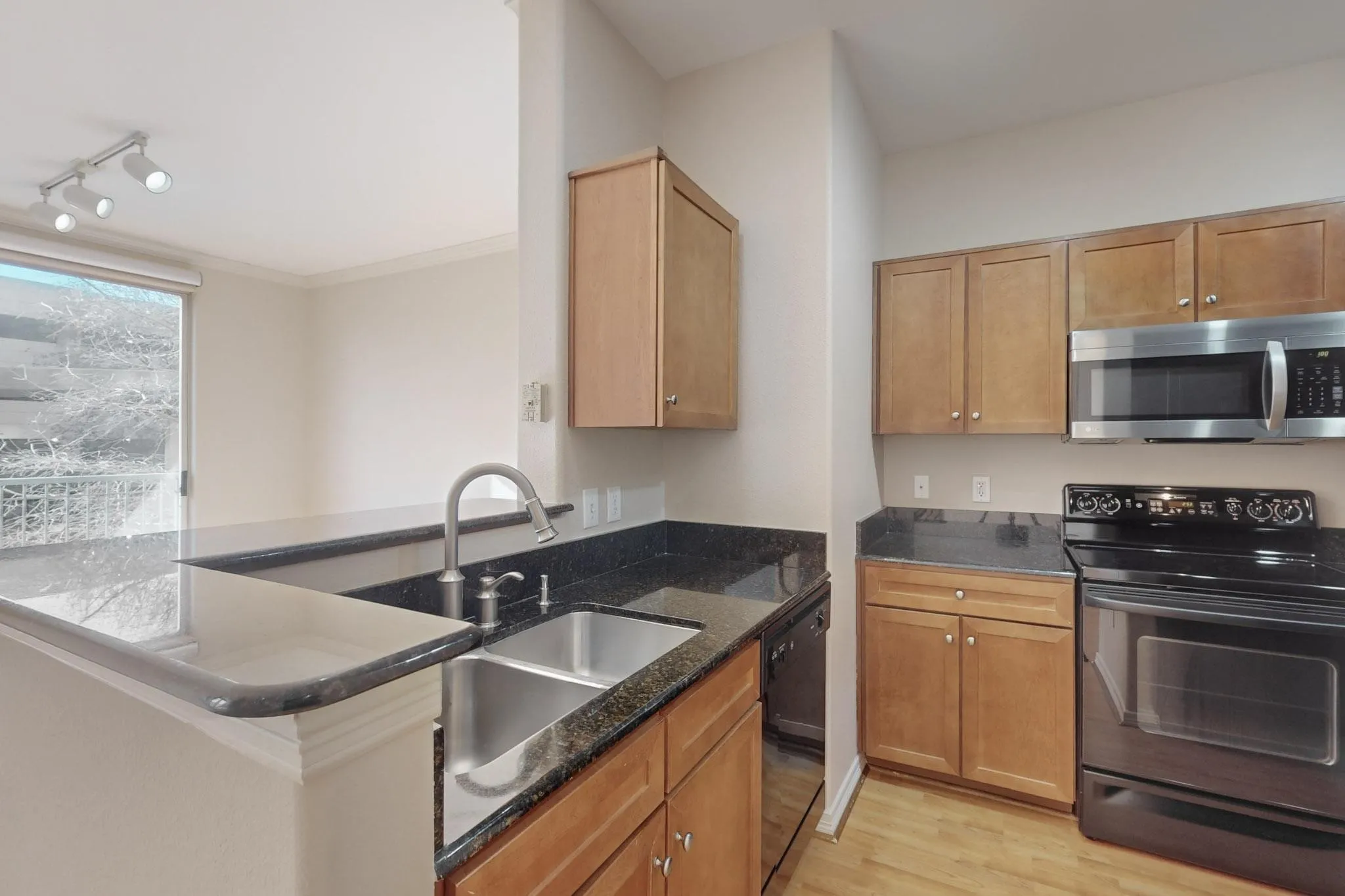 Kitchen with black appliances, dark stone countertops, light wood-style floors, track lighting, and ornamental molding