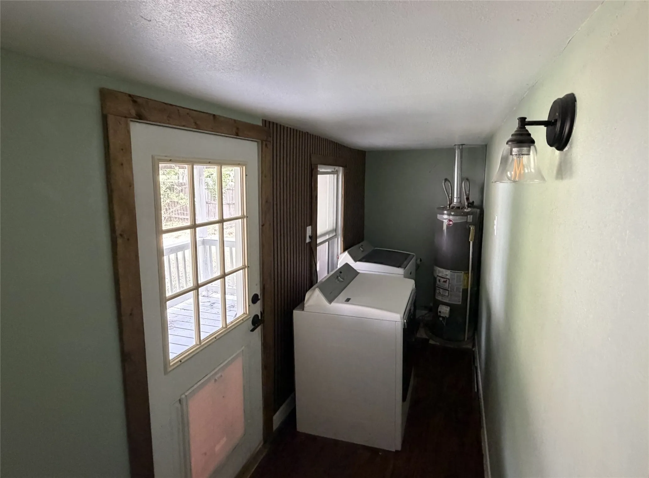 Dedicated laundry area featuring a water heater, a window, wood-finish flooring, and a glass-paneled door with natural wood trim providing exterior access