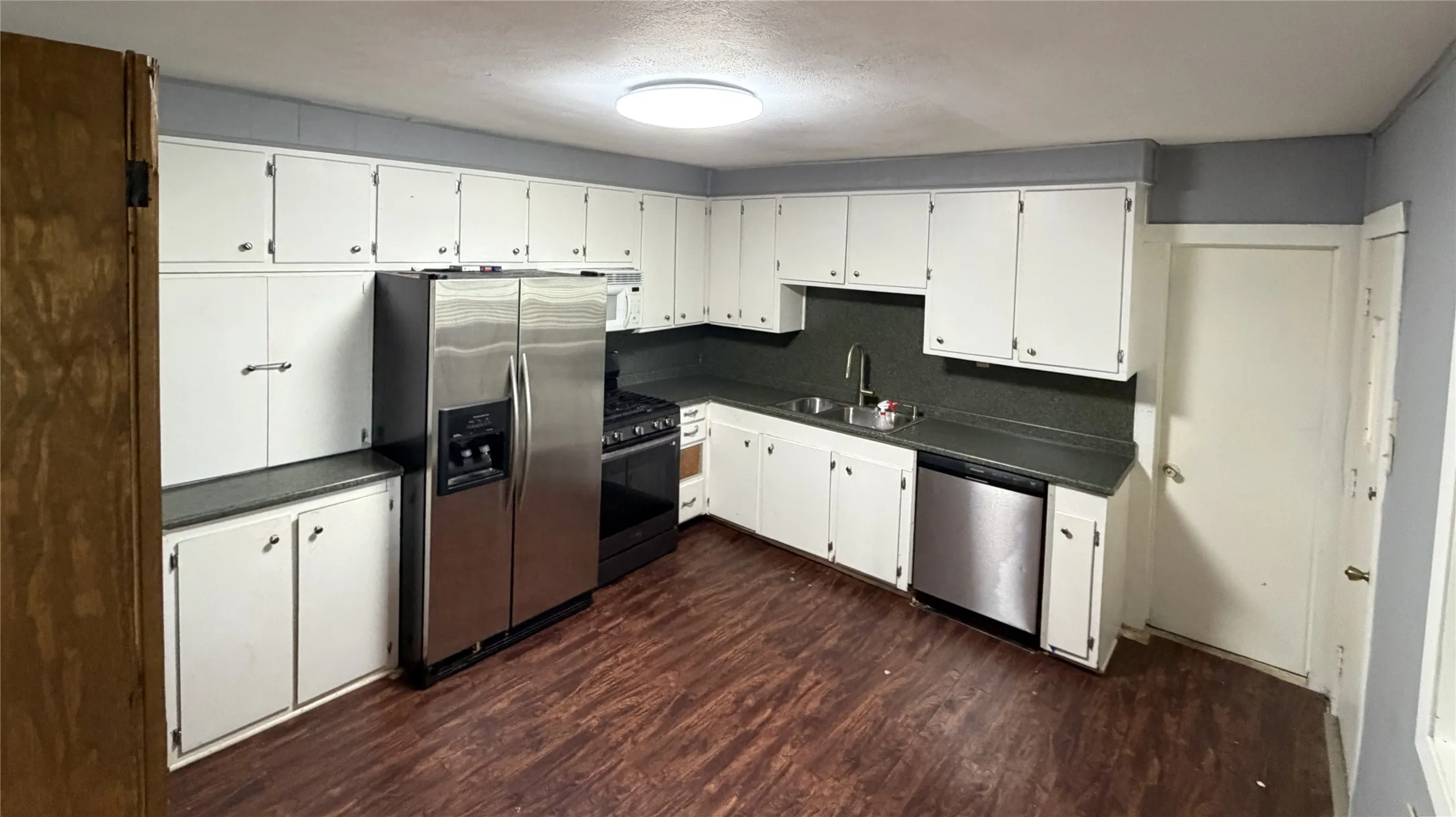 Kitchen featuring white cabinetry, dark countertops, wood-finish flooring, and a stainless steel appliance suite including a refrigerator, range, and dishwasher