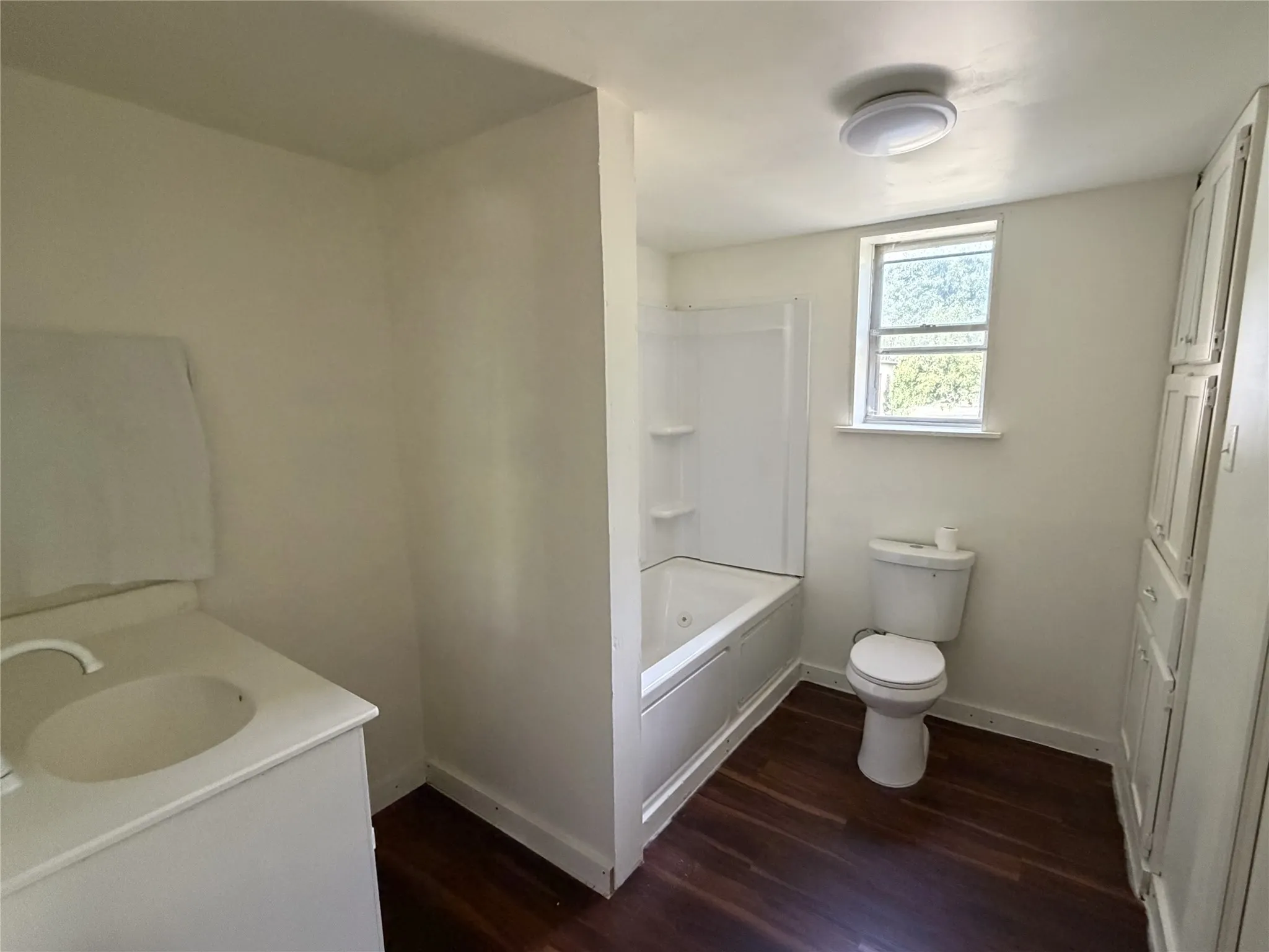 Bathroom featuring a wood-finish floor, built-in storage cabinetry, a vanity with an integrated sink, and a combination tub and shower unit
