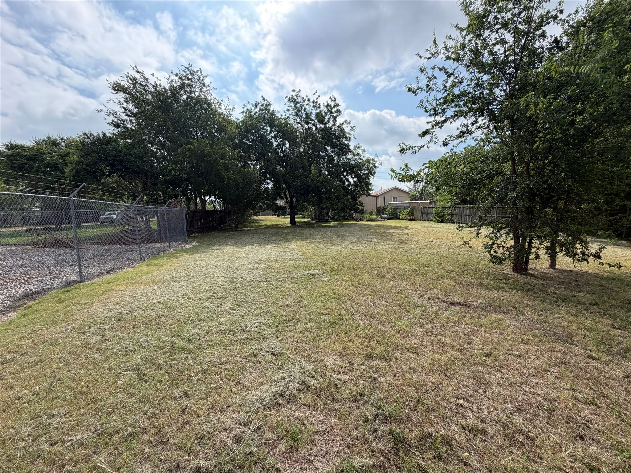 Expansive grassy lot featuring mature trees and a chain-link fence