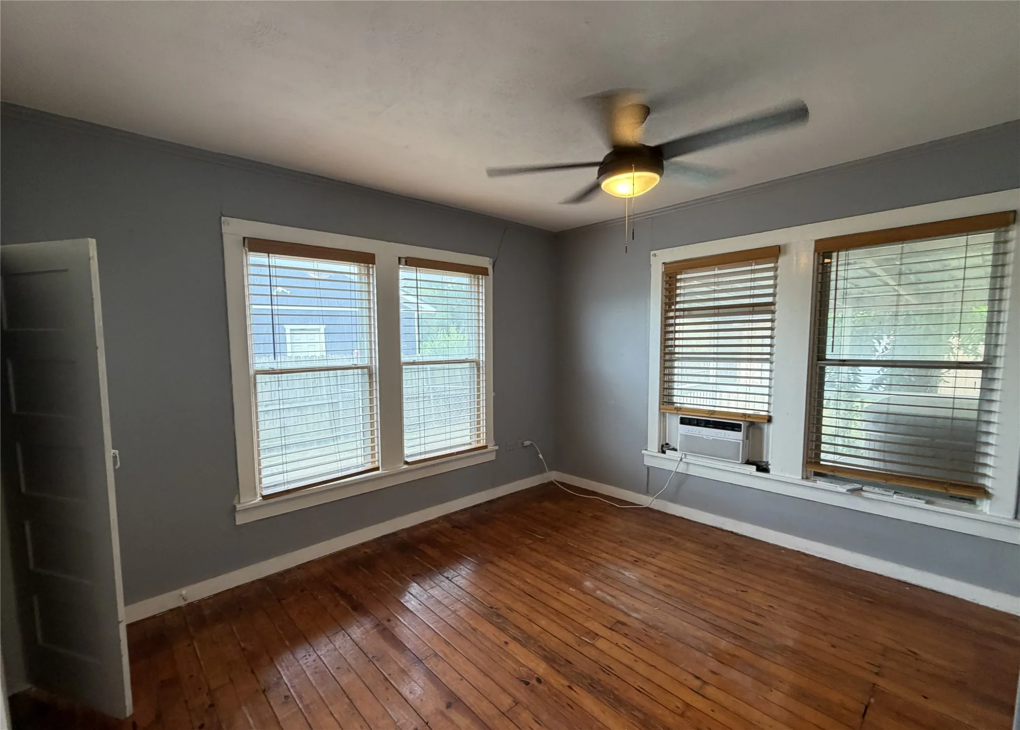 Spacious room featuring wood-finish flooring, light grey painted walls, white trim, and two large windows with blinds