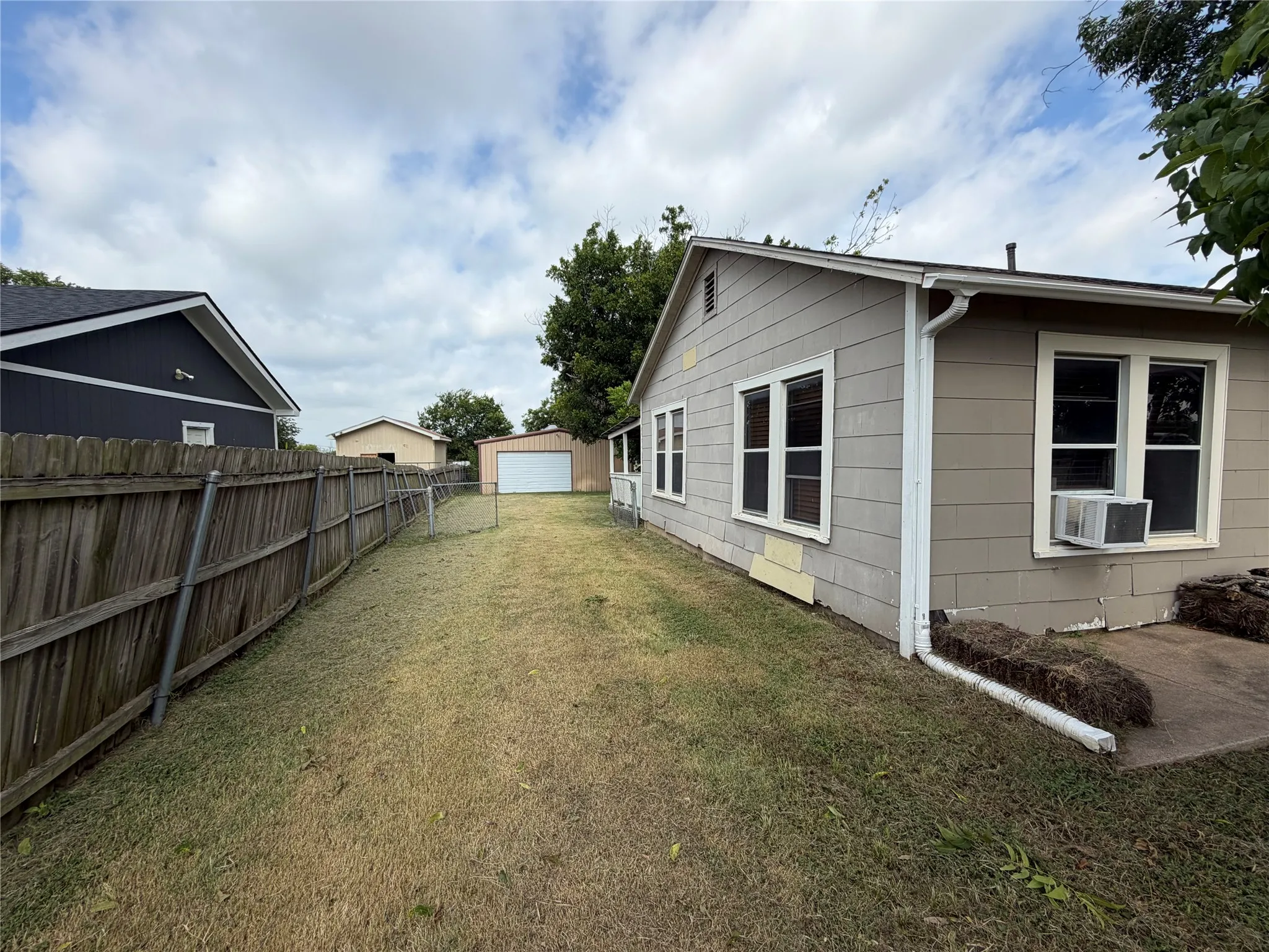 Expansive backyard featuring a wood privacy fence, a detached garage with a white roll-up door, and mature trees