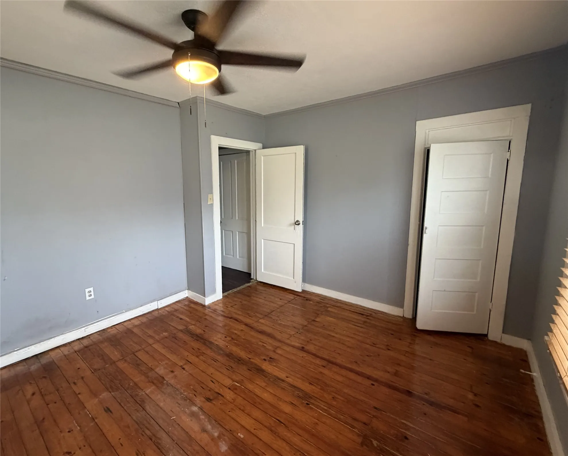 Room featuring wood-finish flooring, two panel doors with hardware, and a ceiling fan with integrated lighting