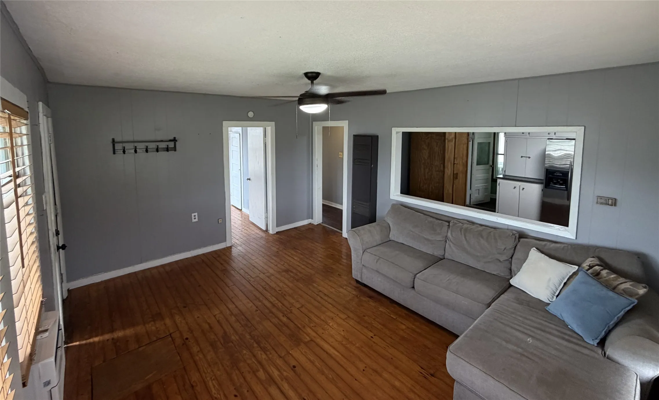 Spacious living area featuring wood-finish flooring, a ceiling fan, and light gray wall paneling