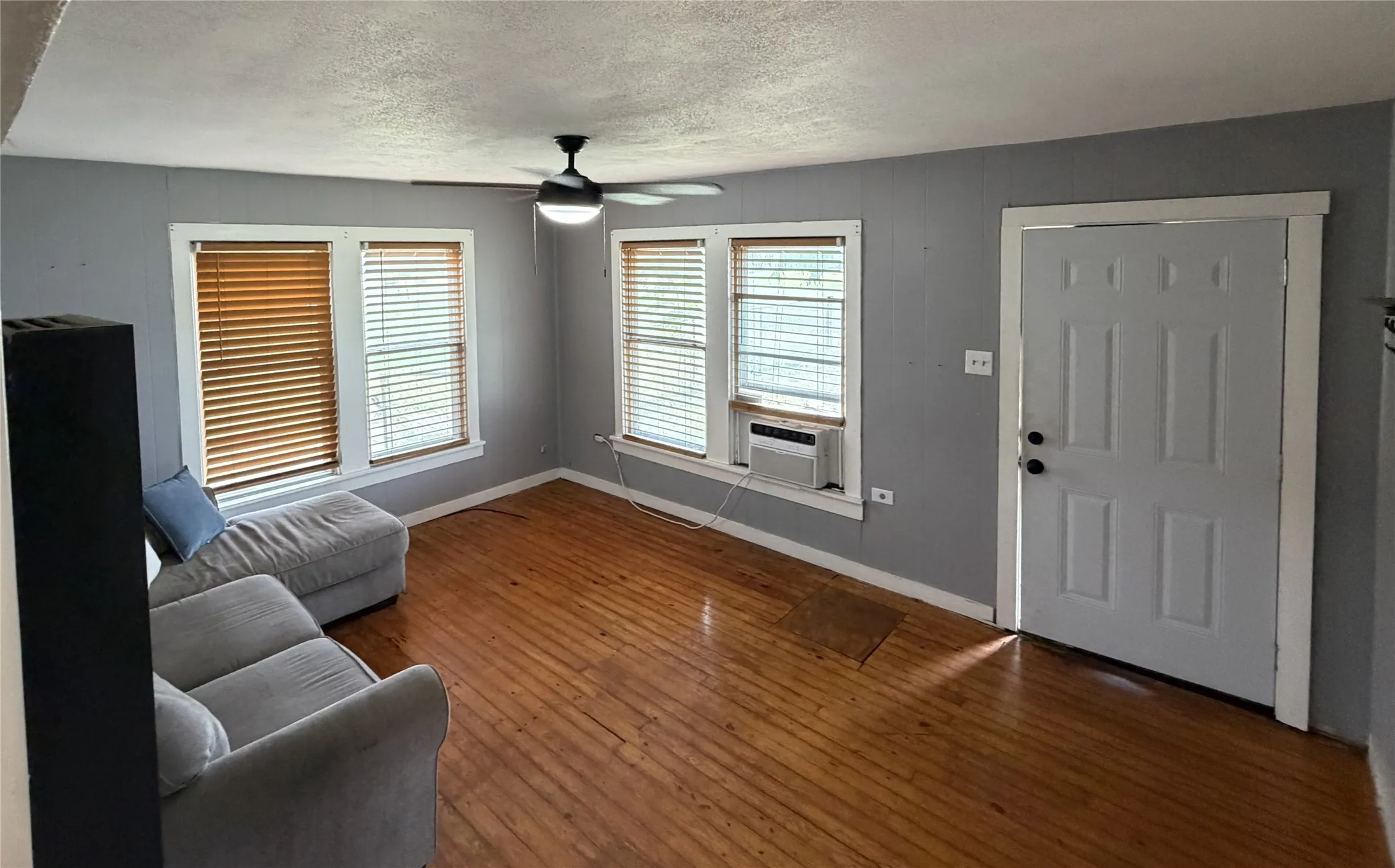 Living area featuring wood-finish flooring, light gray walls, and multiple windows with blinds
