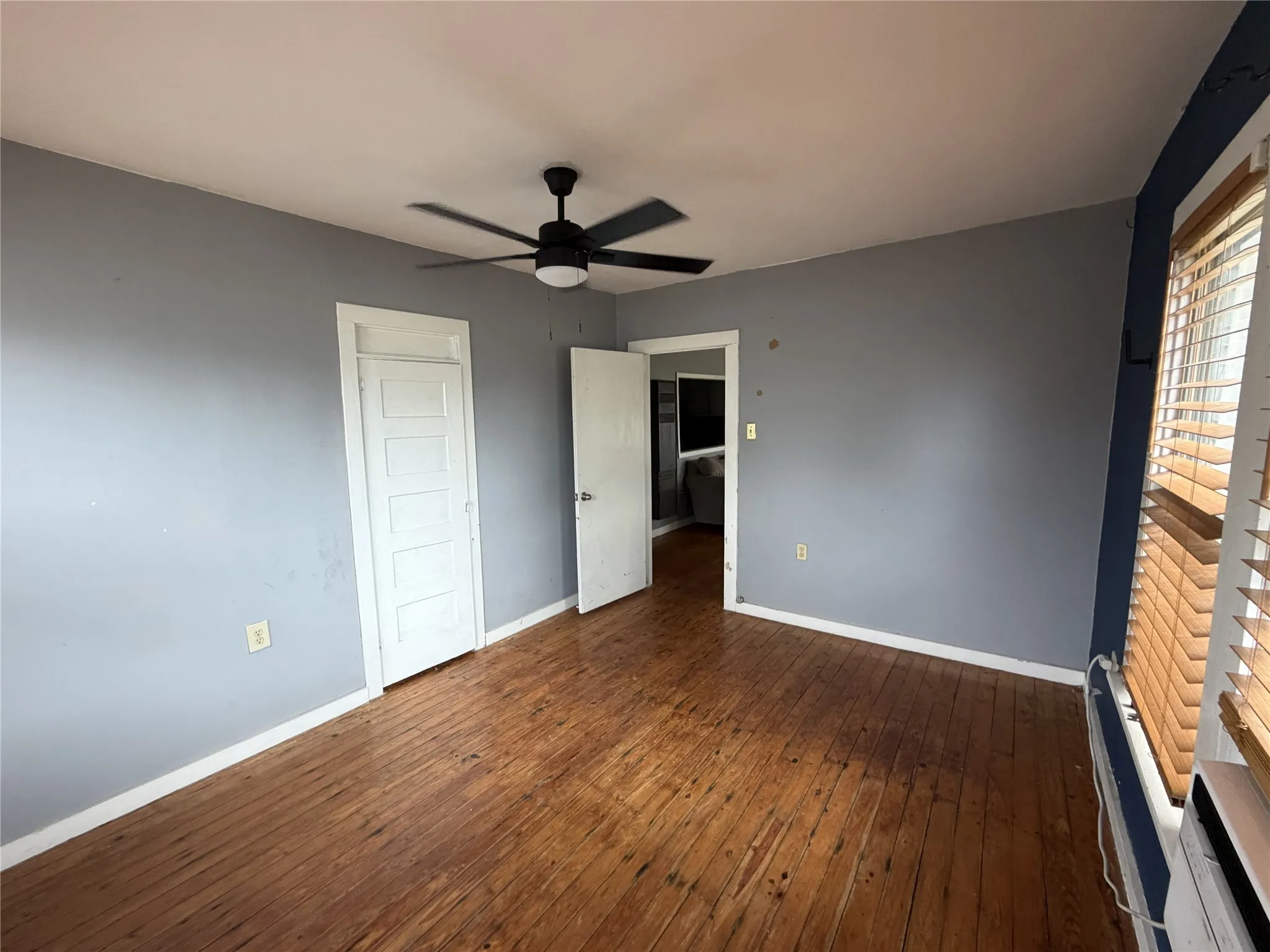 Hardwood flooring throughout featuring a ceiling fan with integrated lighting, window with horizontal blinds, and paneled doors