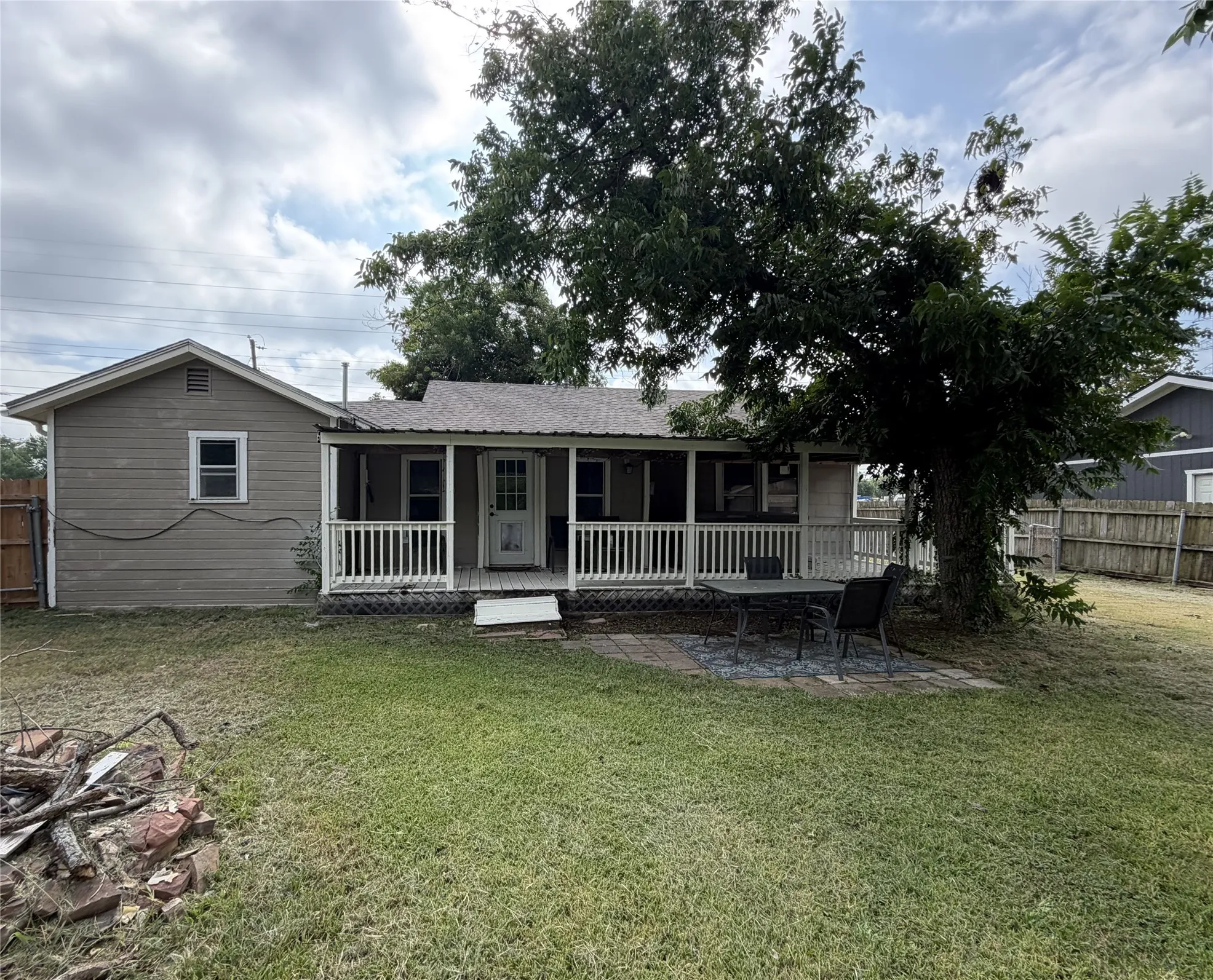 Expansive backyard featuring a covered porch with white railing, paved patio area, and a large mature tree providing natural shade