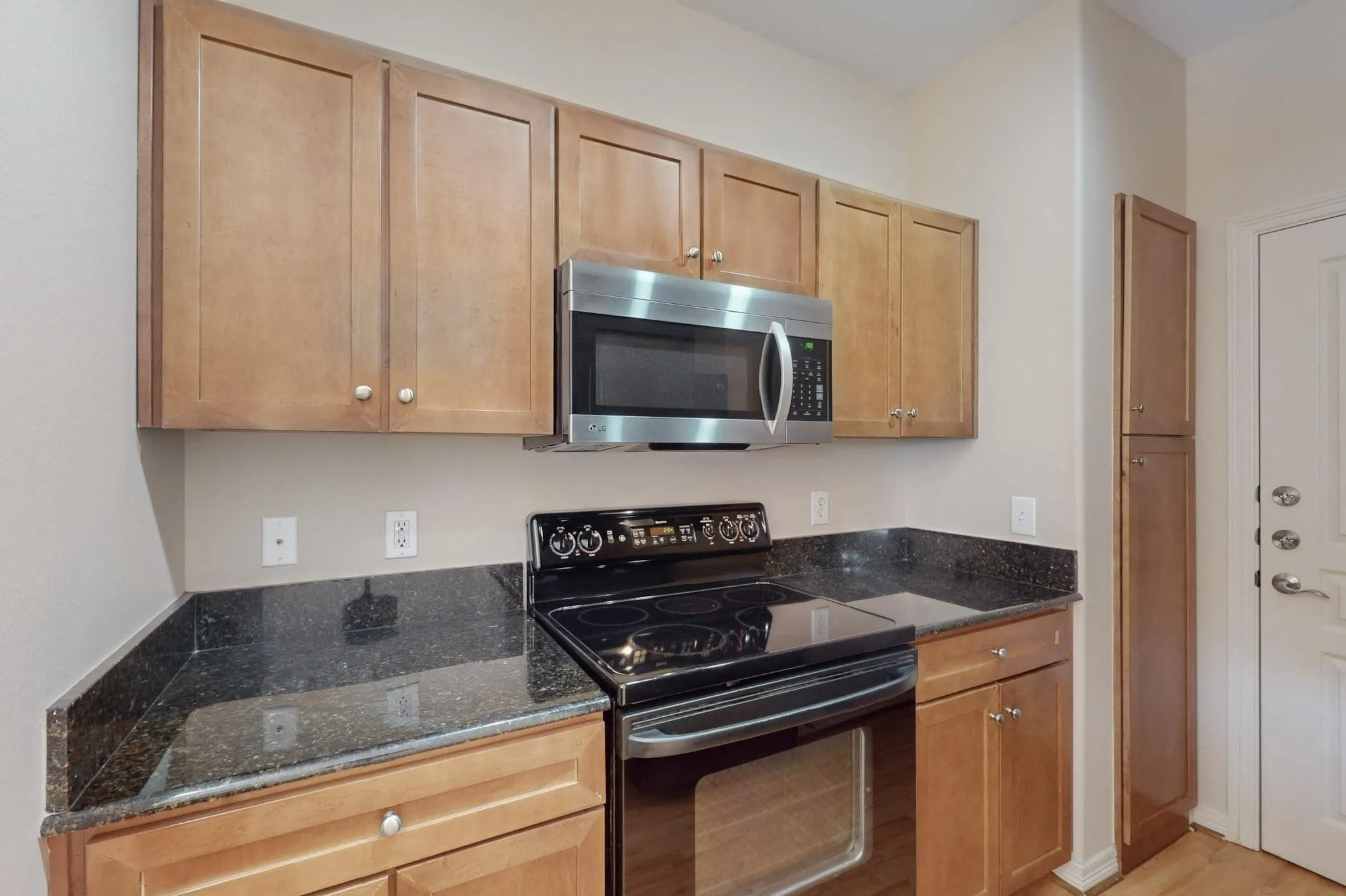 Kitchen featuring black range with electric cooktop, dark stone counters, stainless steel microwave, and light wood-type flooring