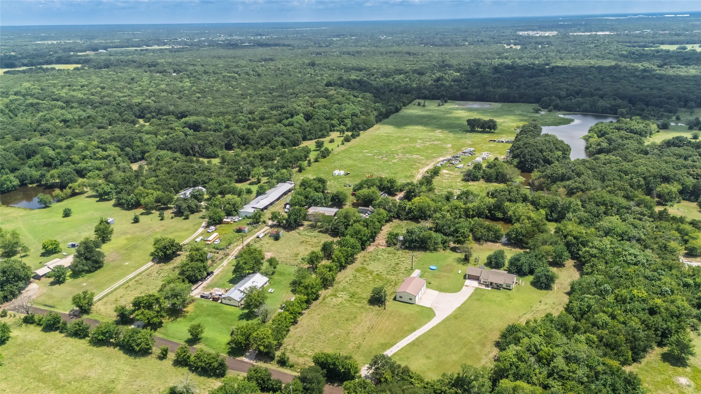 Expansive rural property featuring a primary residence with an attached garage, a separate outbuilding, a long paved driveway, multiple ponds, and abundant tree coverage