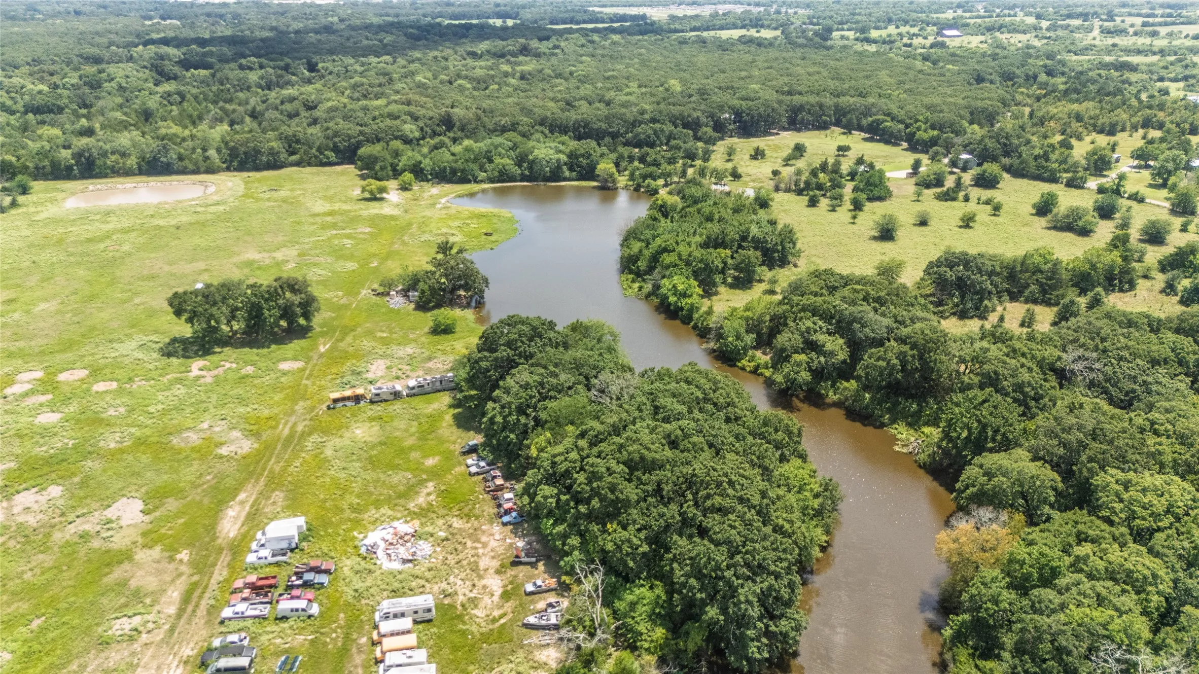 Expansive rural landscape featuring a winding river, mature tree cover, open grassy areas, and a visible pond
