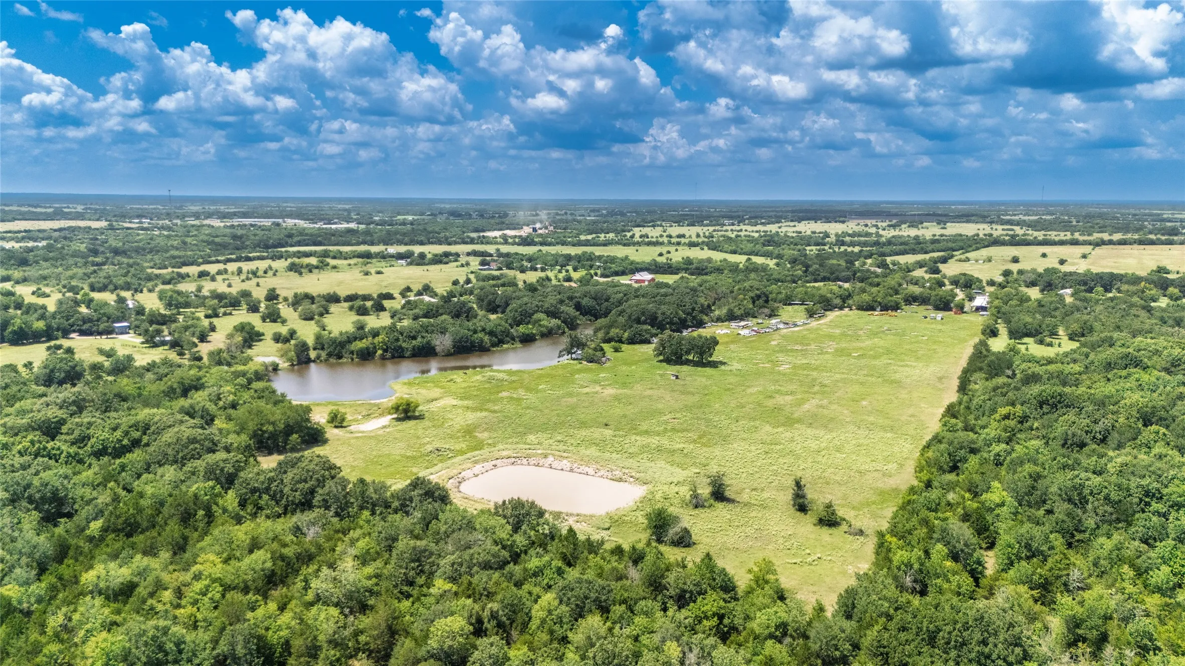 Expansive rural landscape featuring a large body of water, a smaller pond, open grassy fields, and extensive tree coverage