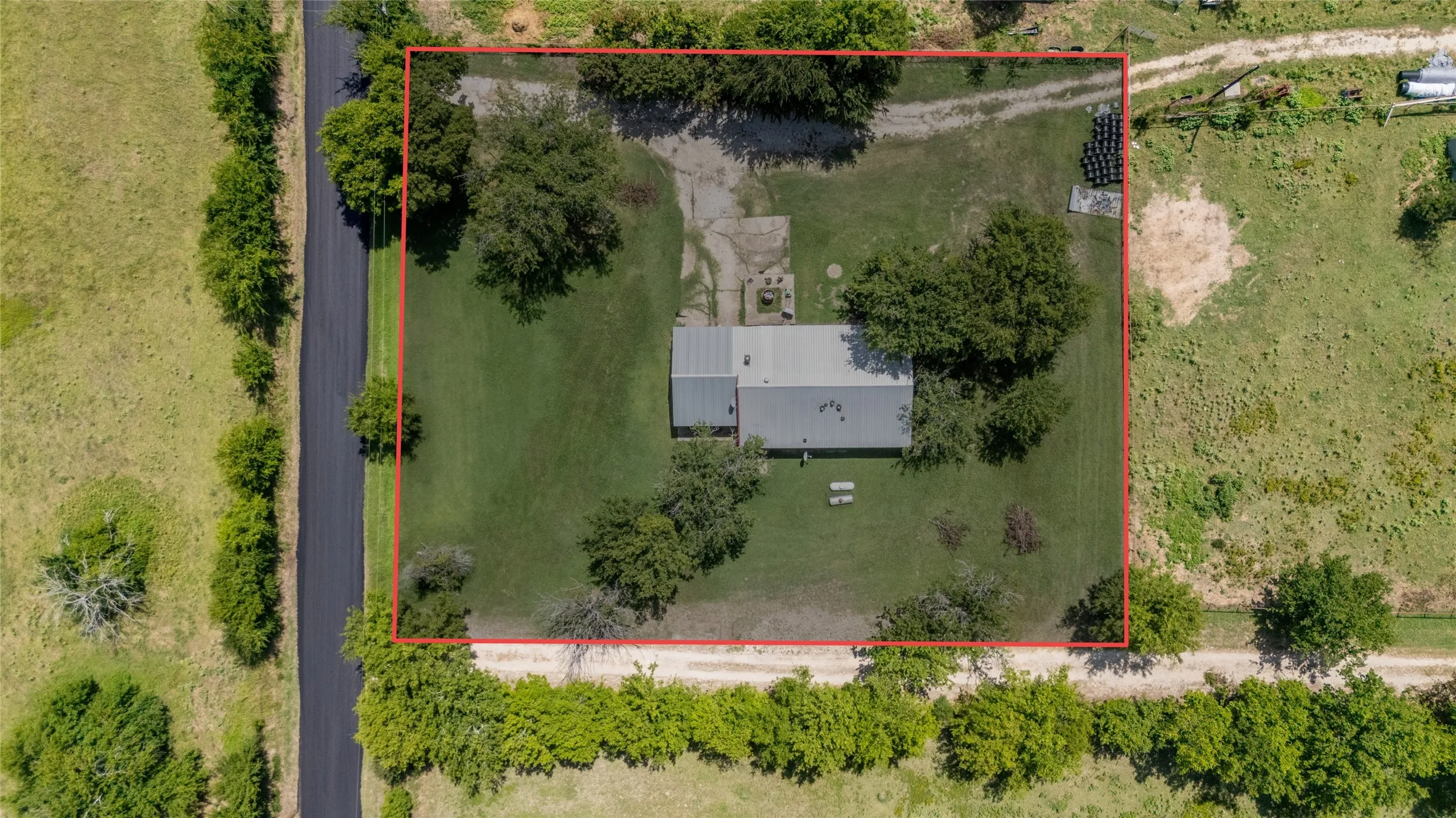 Spacious lot featuring a single-story residence with a metal roof, mature trees, and a paved road frontage