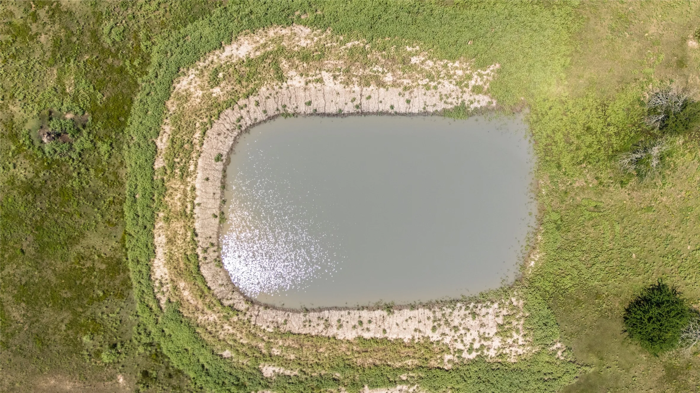 Rectangular water feature surrounded by tiered earthworks and natural vegetation