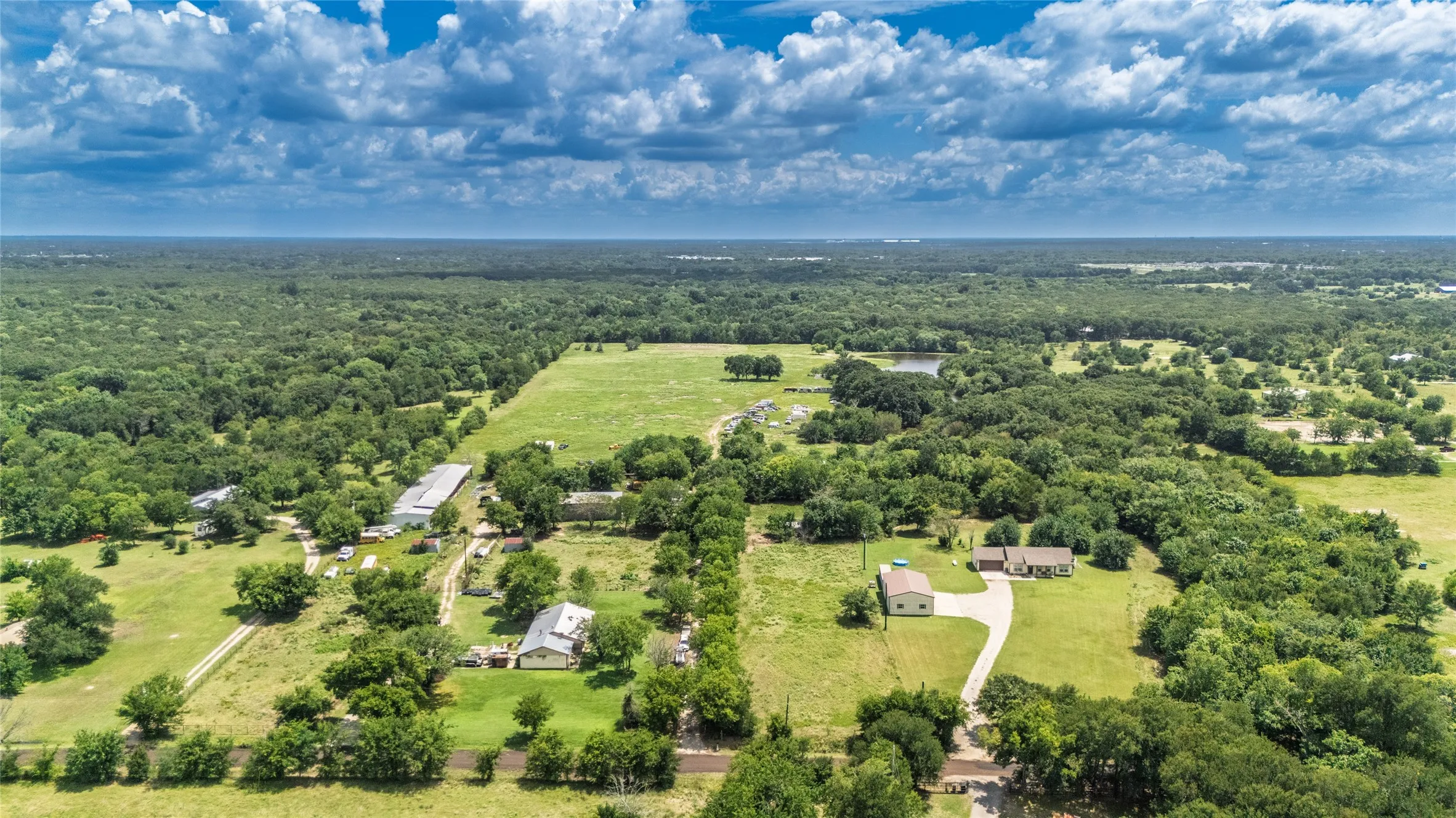 Expansive property featuring multiple structures, cleared pasture land, wooded areas, and a visible pond