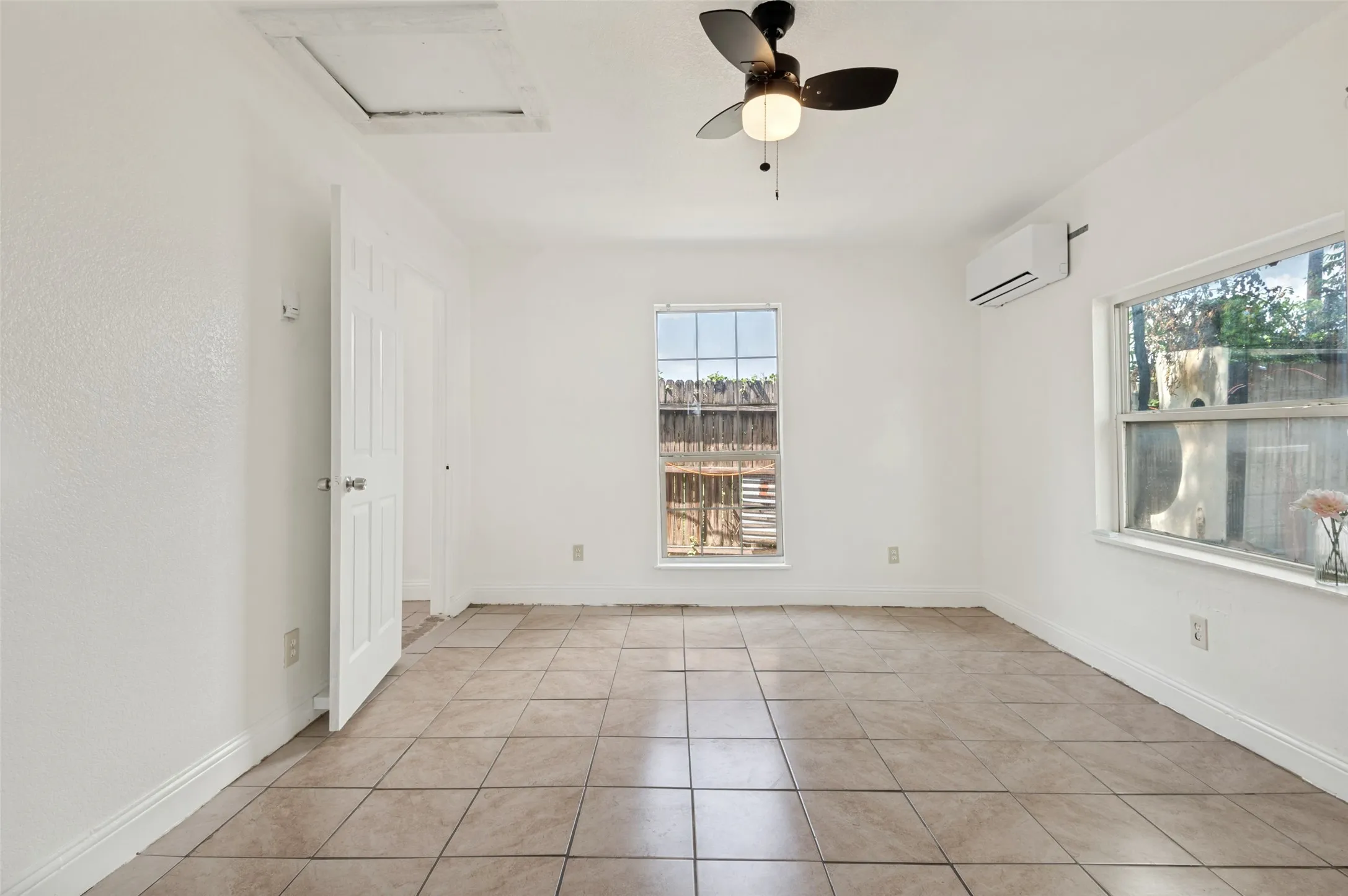 Bright room featuring neutral tile flooring, white walls, two windows, and a ceiling fan with integrated lighting