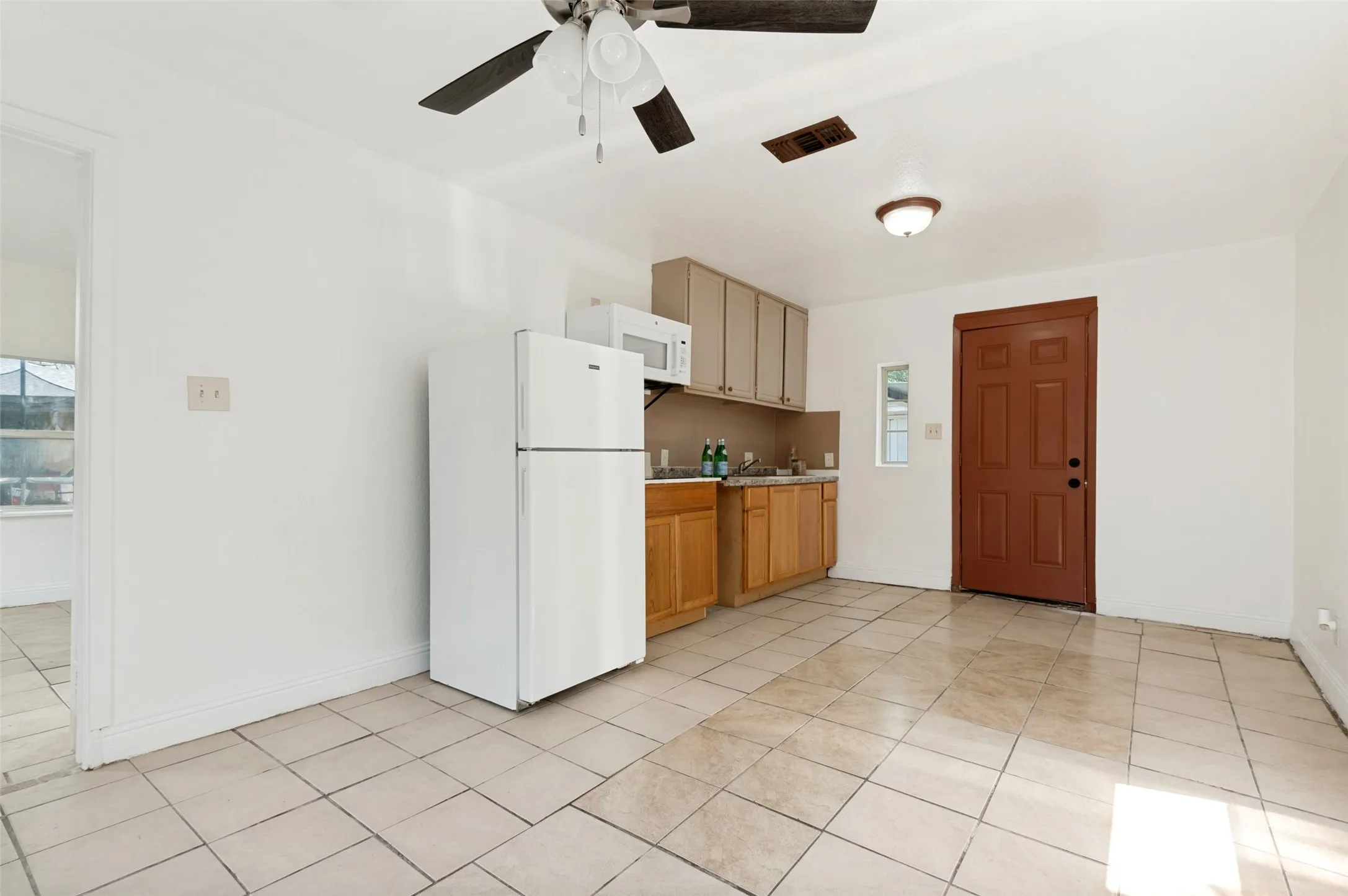 Tile flooring with a compact kitchen featuring wood-finish lower cabinetry, light-colored upper cabinetry, and a ceiling fan