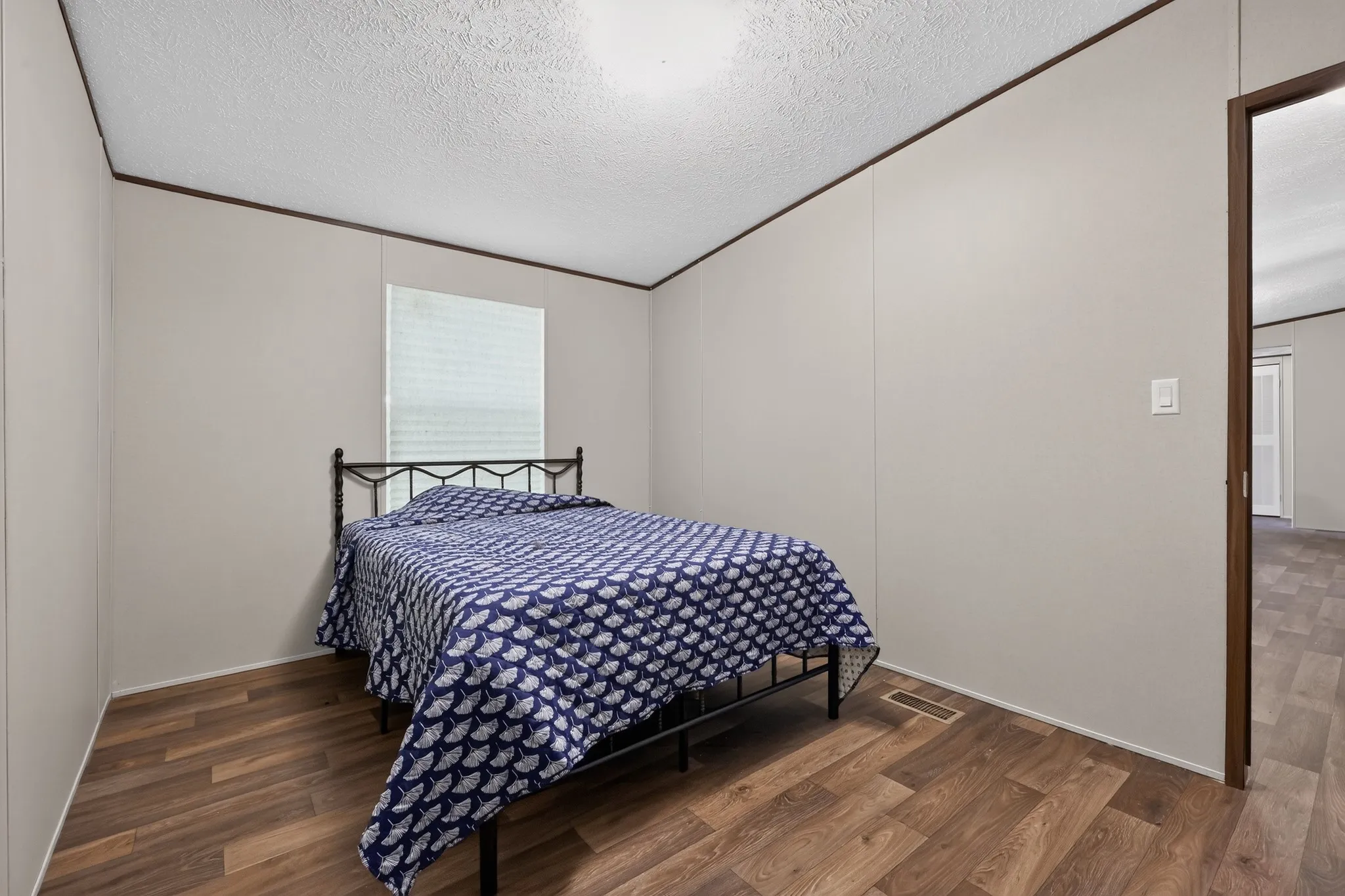 Room featuring wood-finish flooring, light-colored wall panels, a window with blinds, and dark trim details