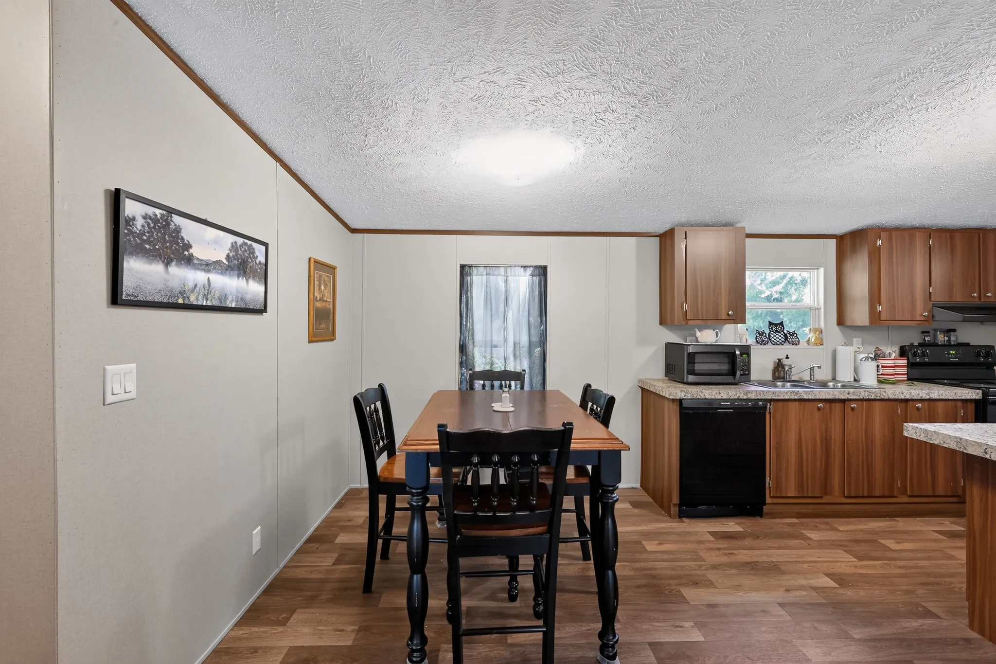 Open-concept kitchen and dining area featuring wood-finish flooring, wood cabinetry, and black appliances