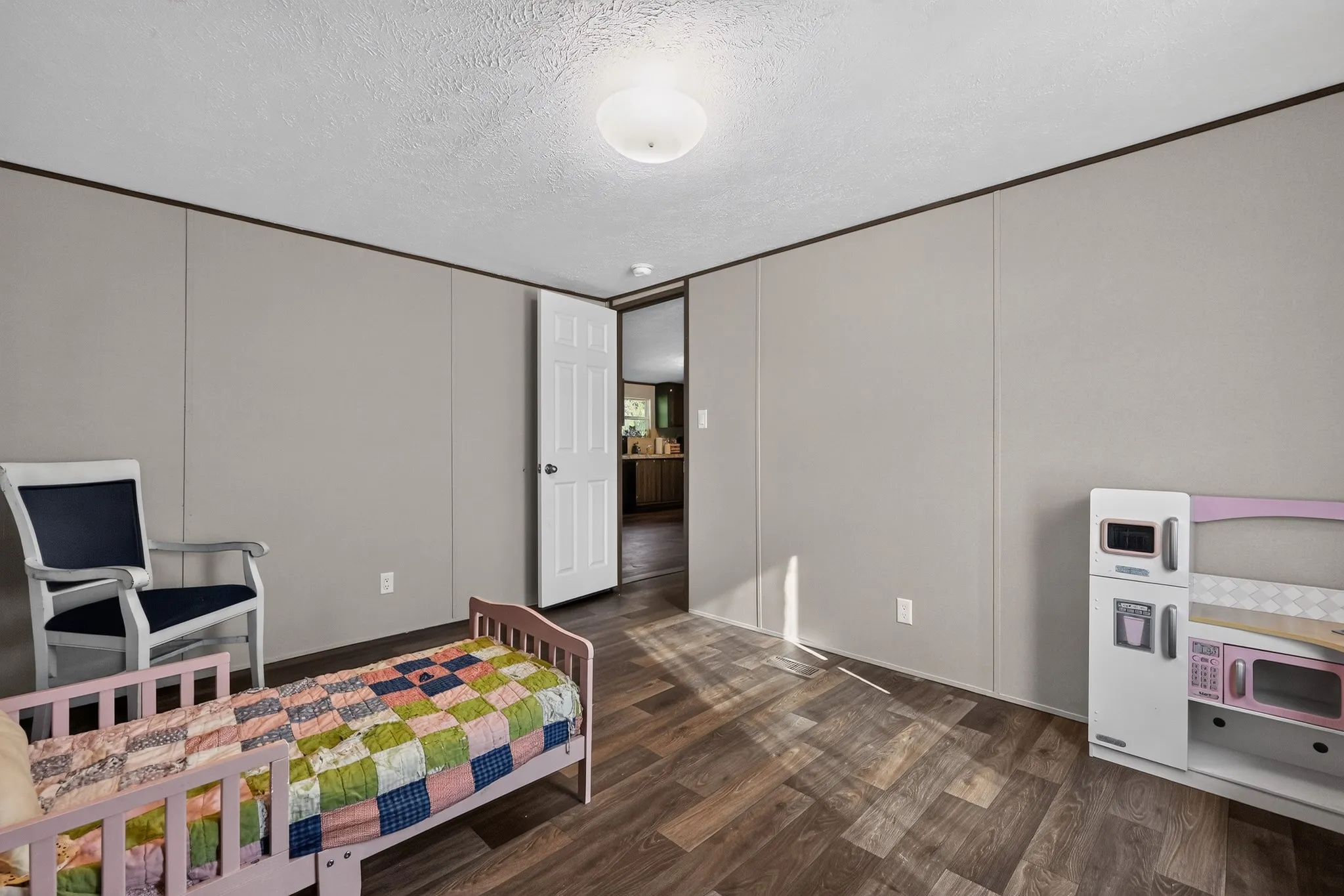 Wood-finish flooring throughout, neutral wall paneling, and a white interior door