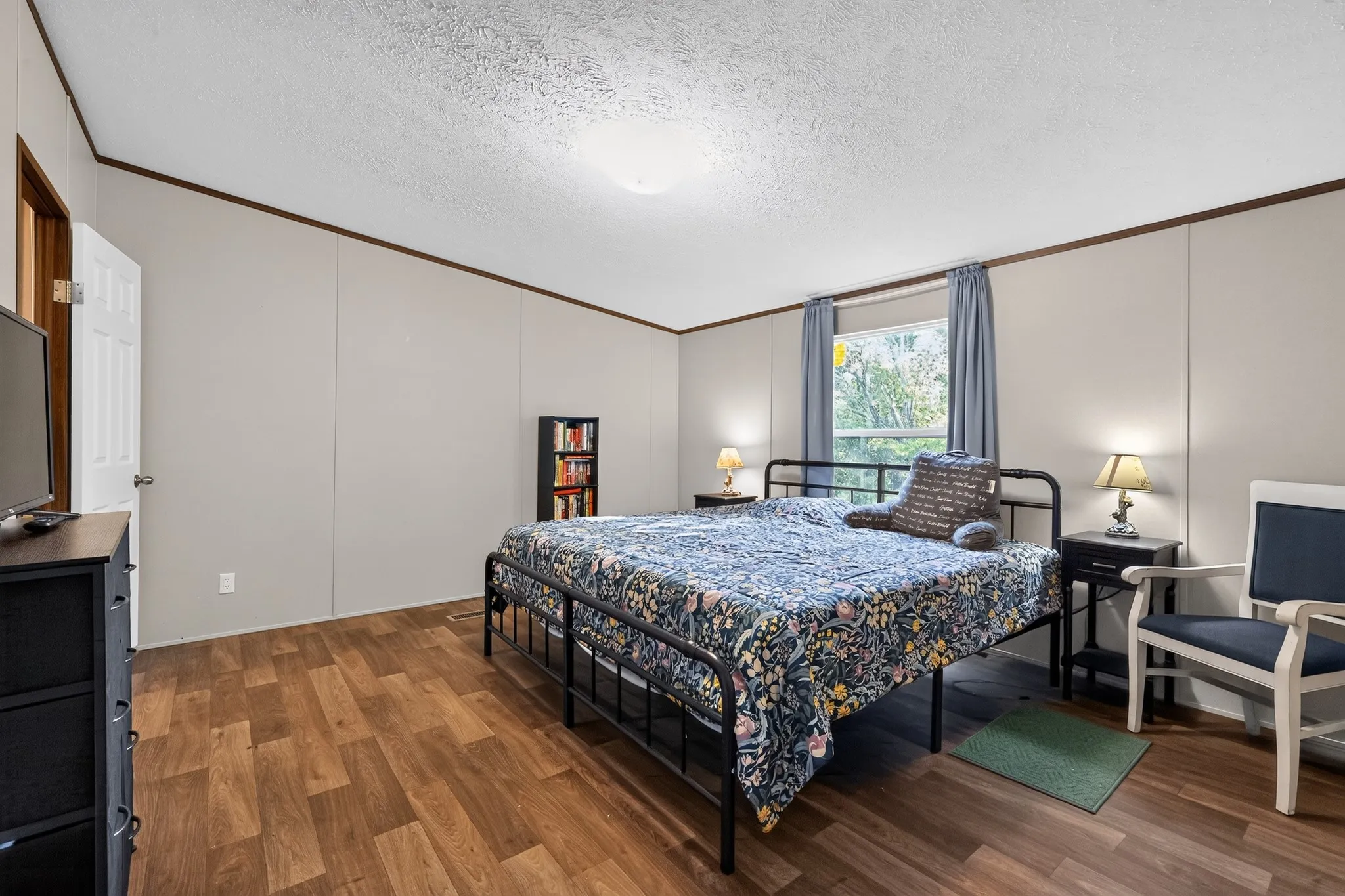 Spacious room featuring wood-finish flooring, light gray wall panels, and a window with natural light