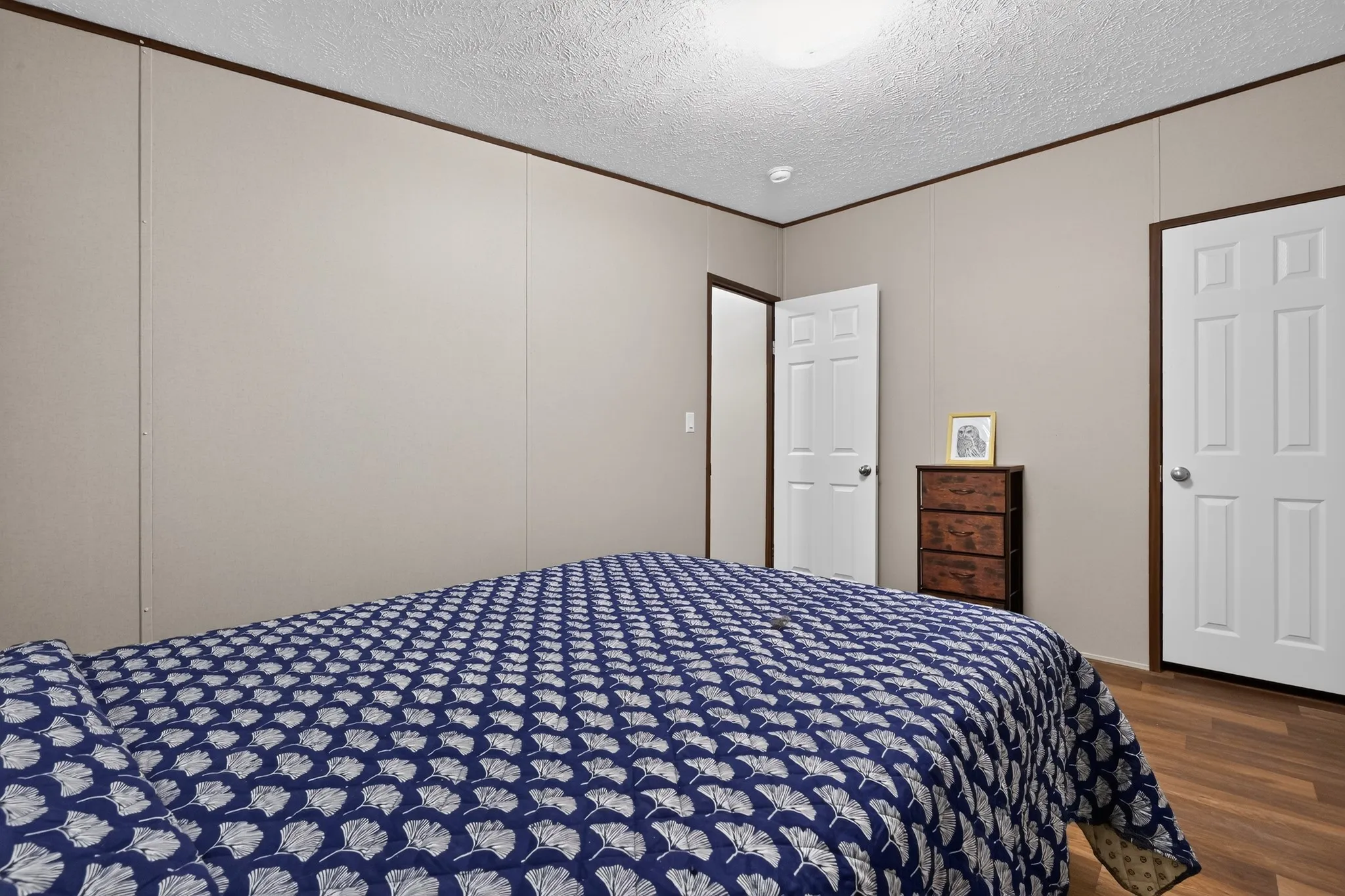 Bedroom featuring neutral wall panels with dark trim, wood-finish flooring, and white paneled doors
