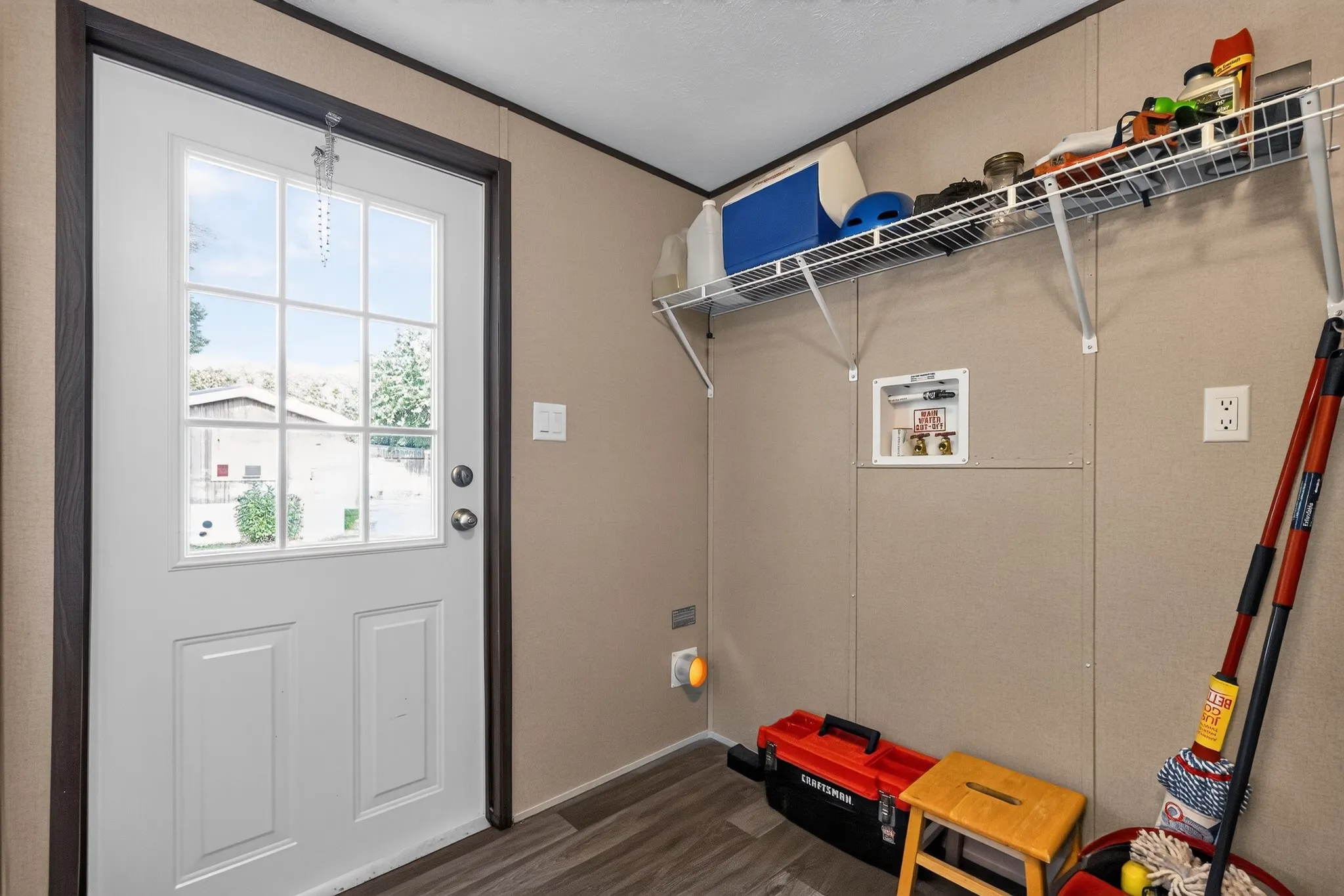 Utility area featuring a paneled exterior door with divided lites, wood-finish flooring, a wall-mounted storage shelf, and a laundry hookup station