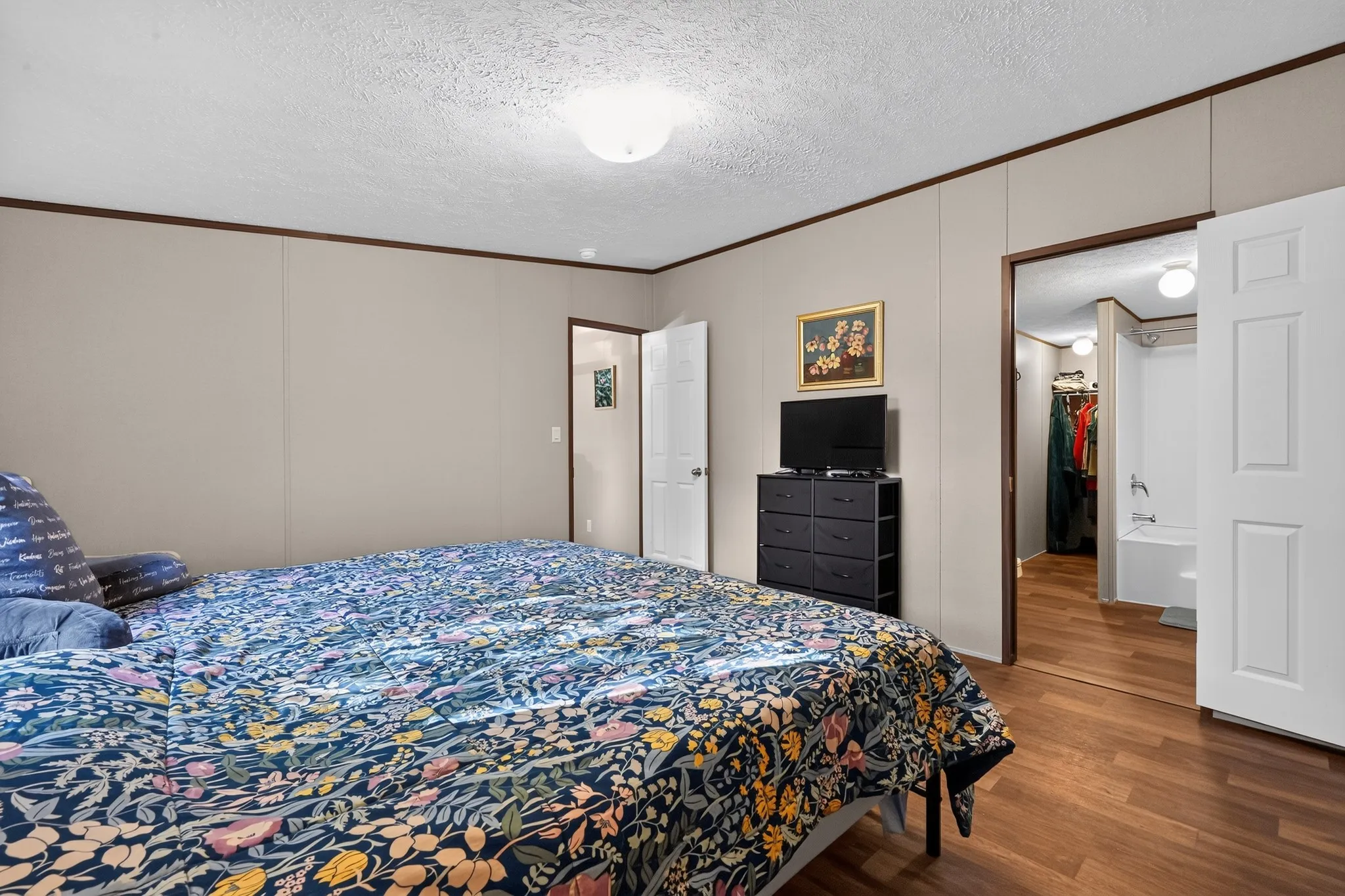 Bedroom featuring wood-finish flooring, light neutral wall panels, and white trim