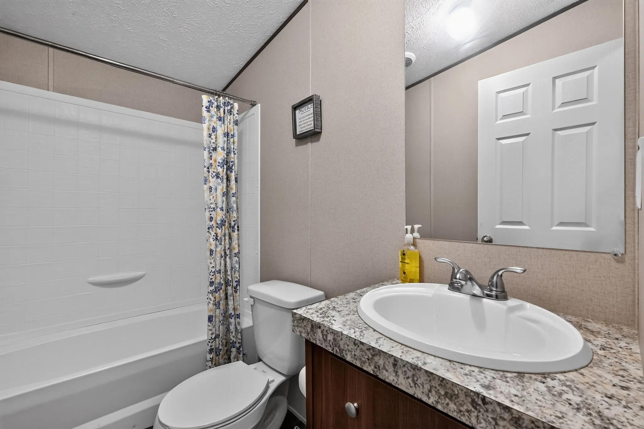 Bathroom featuring a built-in tub with shower, wood-finish vanity with an integrated sink, and a speckled countertop