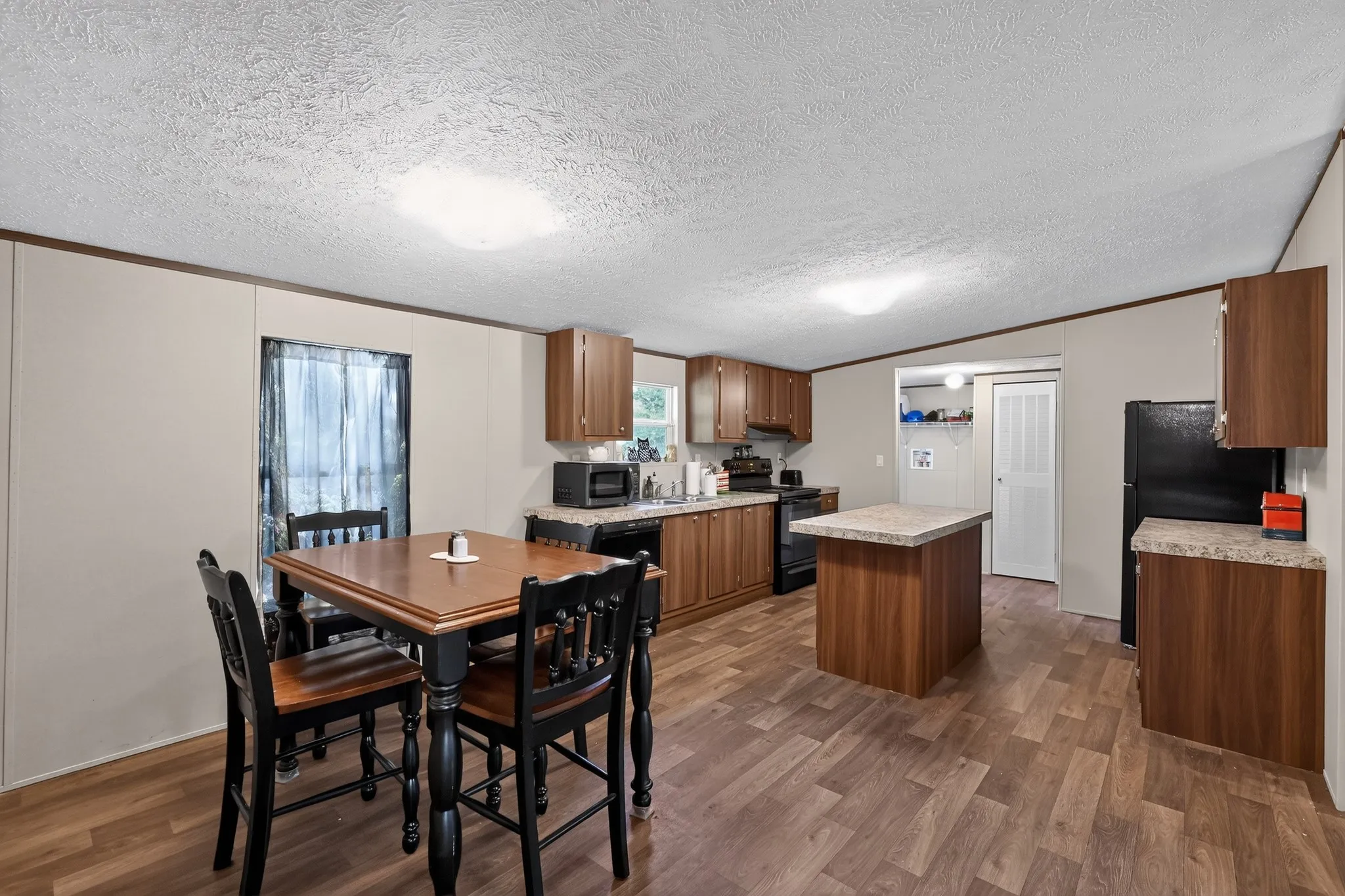Open-concept kitchen and dining area featuring wood-finish flooring, wood cabinetry, stone-finish countertops, and a central island